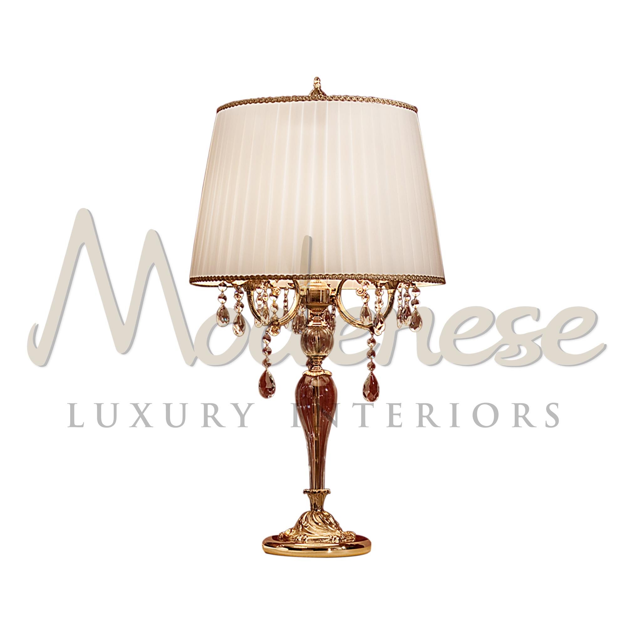 Die Designer von Modenese Luxury Interiors haben diese Tischleuchte mit einer 24-karätigen, antik vergoldeten Struktur, wunderschönen Kristallanhängern in Scholer und eleganten Stoffen gestaltet. Dieses Modell benötigt 3 einzelne