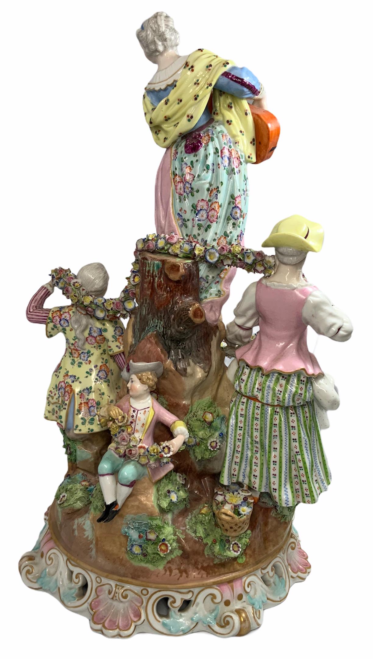 Large Rococo porcelain figure group depicting a scene of peasants, a young woman playing a guitar in the top of a rock accompanied by a young couple and a little girl who are holding a garland of flowers around her. The whole sculpture is painted
