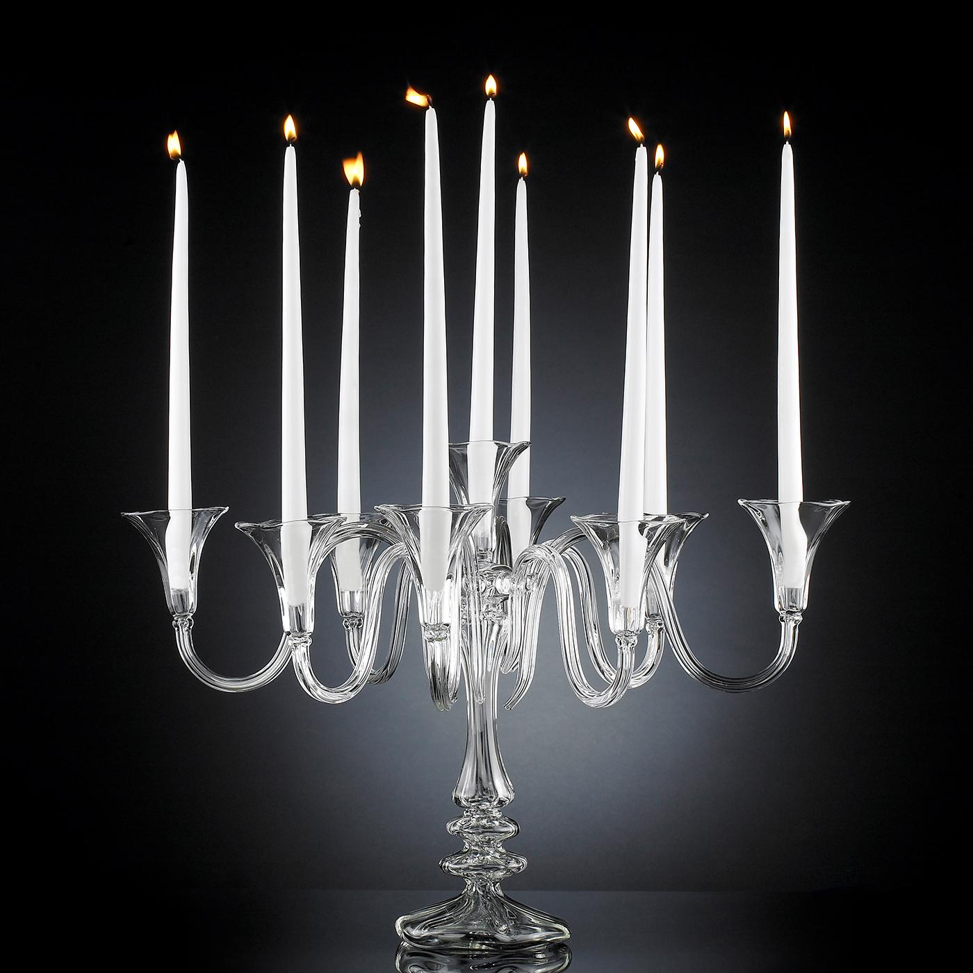 Characterized by nine sinuous arms, this splendid candle holder will make a refined statement when displayed at the center of an elegant dining table of both modern or classic inspiration. Masterfully handcrafted of glass, its natural transparency