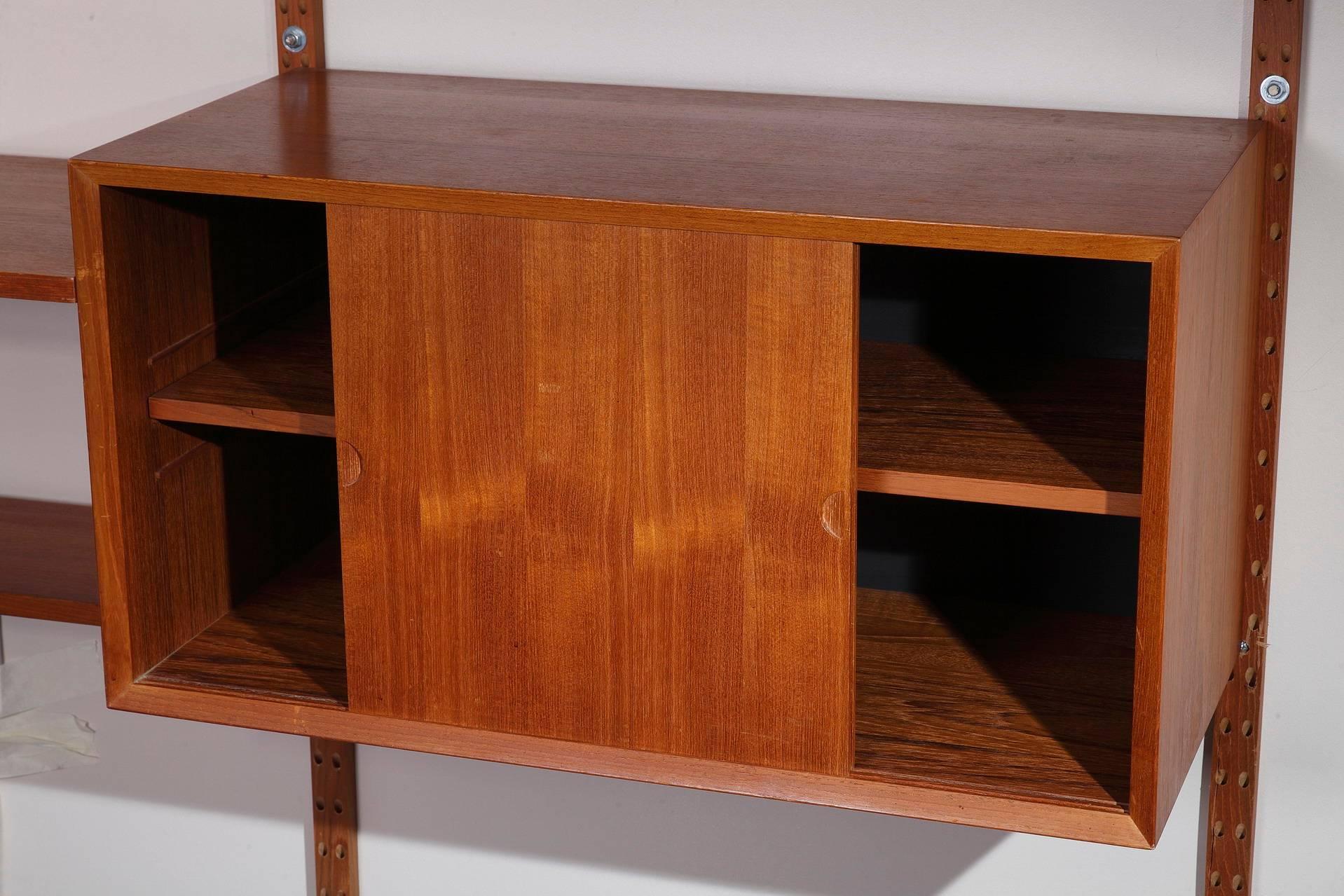 Poul Cadovius Royal System wall unit system in teak from the 1950s. It is composed of four vertical ladders with six shelves and three containers as follow: one container with lateral doors, one container with a flap and storage for magazines, and
