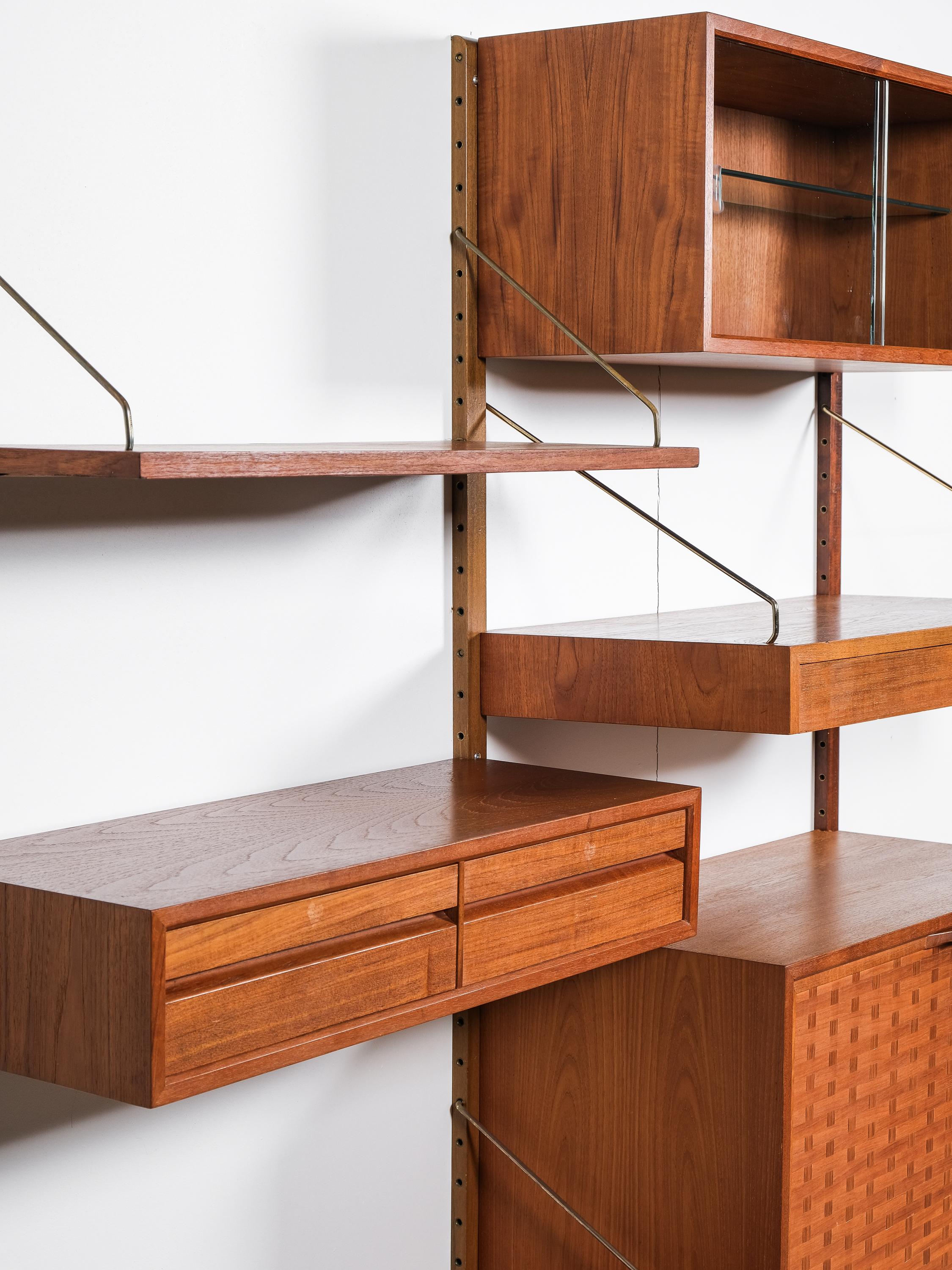 Great Danish modern teak wall unit ”Royal System” designed by Poul Cadovius, circa 1950s. 

This piece contains 2 shelves, one cabinet with glass sliding doors, one with drop-down door and two drawers. This piece is completely adjustable, and any of