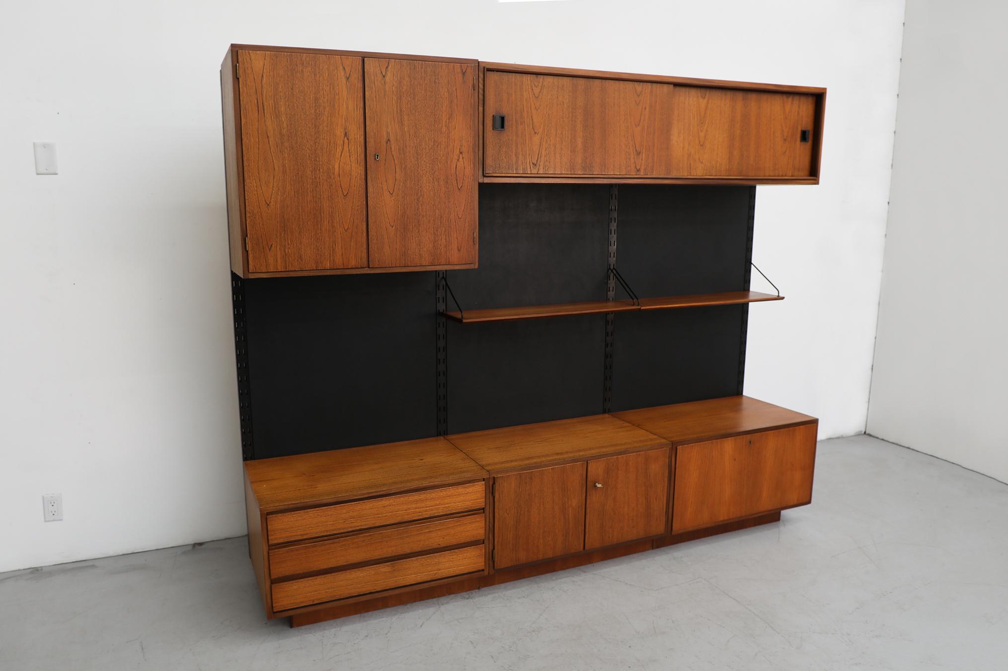 Rare midcentury free standing teak Royal System wall unit by Poul Cadovius. This modular piece has three connecting black vinyl back boards with risers on each side. The system includes two shelves, and five cabinets including some with locking