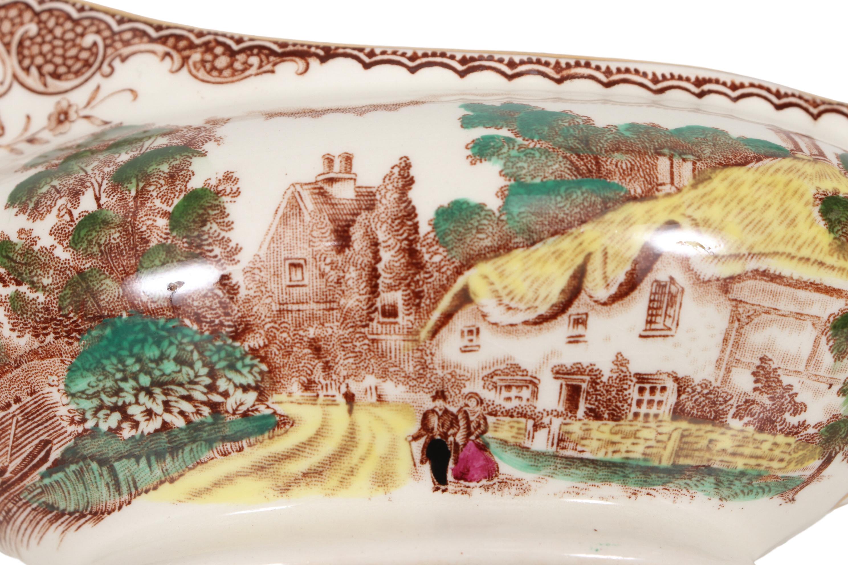 An English transferware porcelain gravy boat made by Barker Brothers. Decorated in their Olde England pattern in brown with yellow, green and some magenta. On one side the pattern shows a Victorian couple in front of a house with a thatched roof. On
