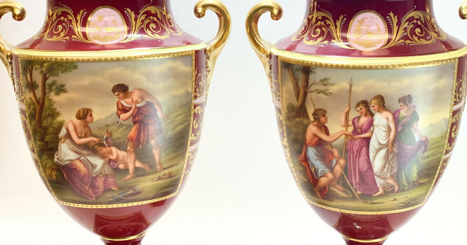 Pair Royal Vienna Austria hand painted porcelain double handled urns, circa 1900. Hand painted portraits to the central area depicting a woman cutting off a cherub's wing, and a courting scene between a man and 3 beauties. Artist-signed 