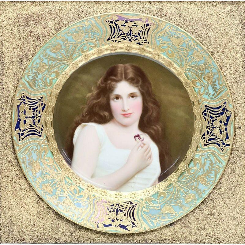 Royal Vienna Austria hand painted porcelain portrait plate beauty Framed, c.1890

Plate with a multi-colored ground with raised gilt floral design and beading. Center depicts a portrait of a beauty holding a purple and white pansy. Artist signed