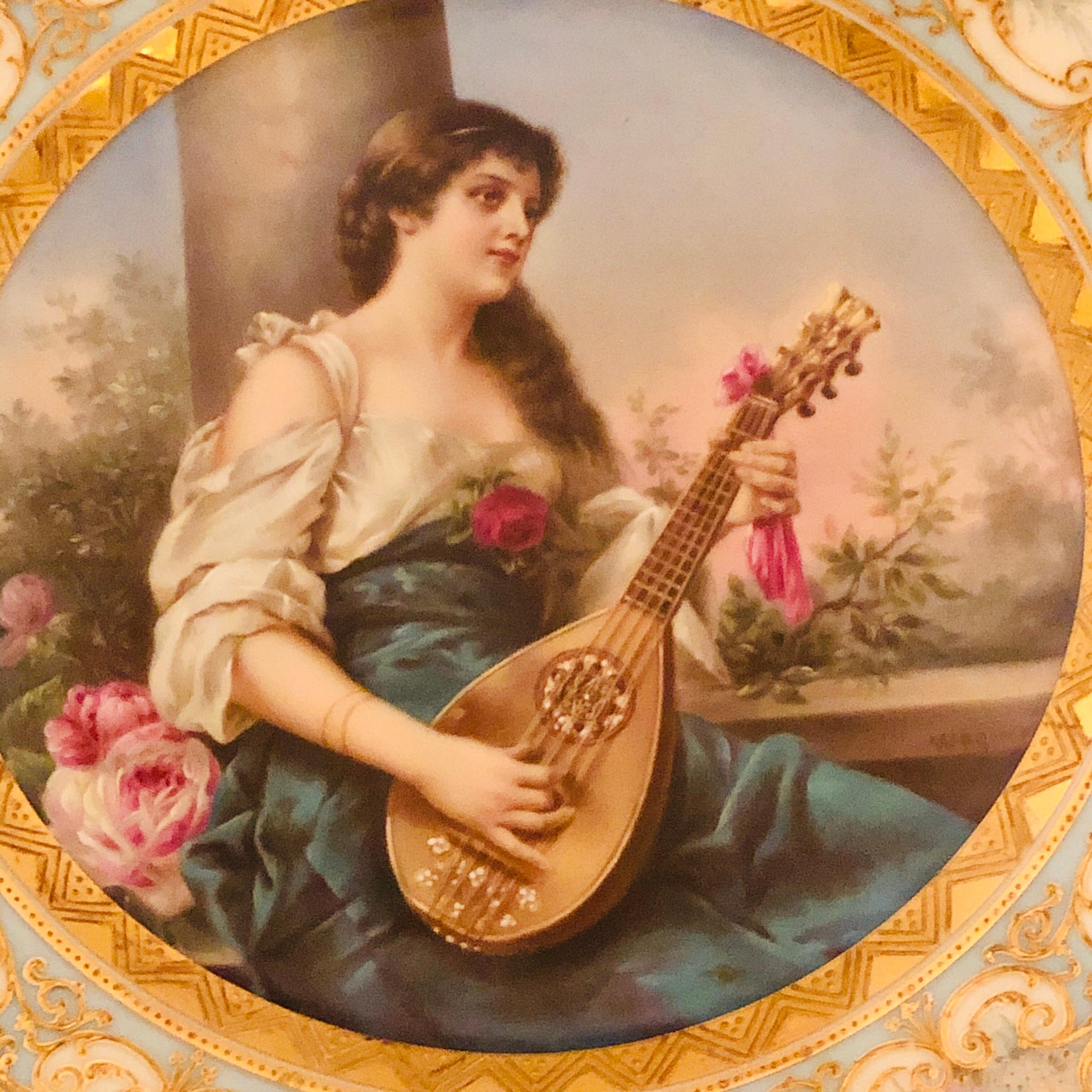 This is a spectacular Royal Vienna plate of a lady playing a mandolin artist-signed Wagner. The border of this plate is decorated with elaborate raised gilding and delicate flowers. This plate is marked with an under glaze blue beehive mark on the