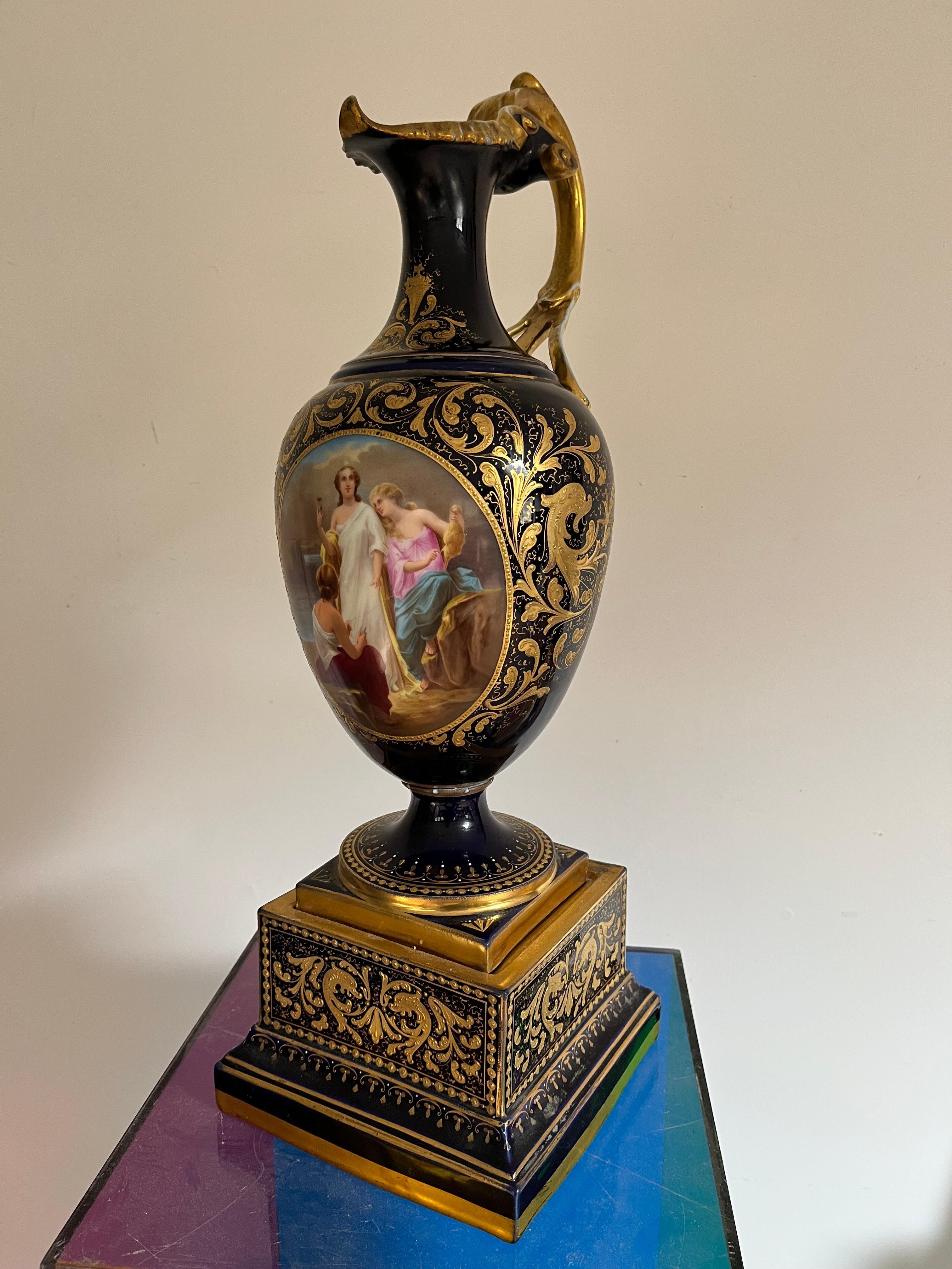 A lovely mid to late 19th century Royal Vienna ewer in deep blue glaze with a pictorial panel depicting two women seated spinning yarn with another woman standing holding an hour glass. The ewer is abundantly decorated with gilt details and the