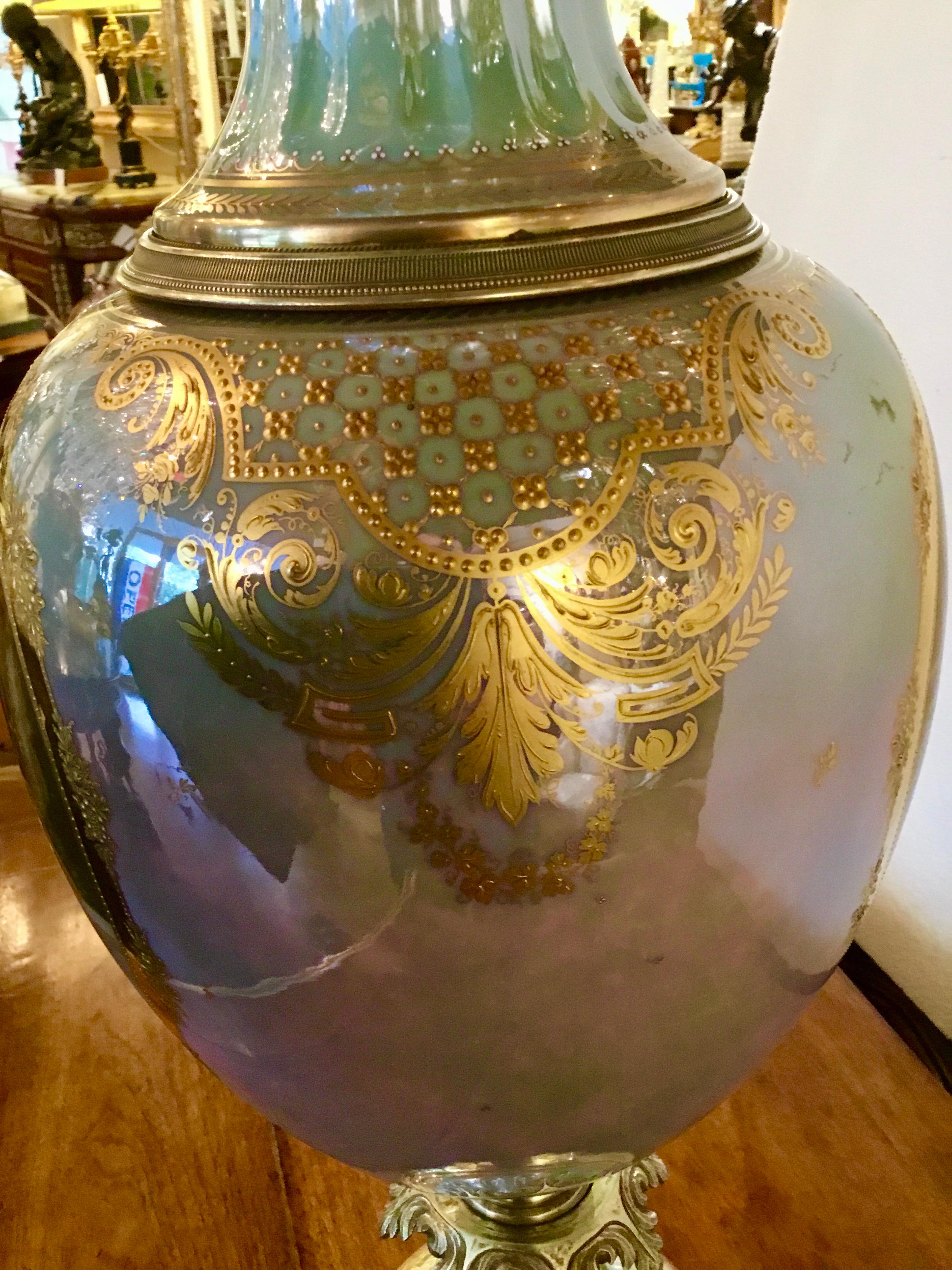 Exquisite porcelain urn with a woman and angel painted n one side
And two women in a garden scene on the reverse side. The background 
Color is a pale aqua hue with a luster glaze. Gilded adornments in a scrolling
Design embellish this piece.