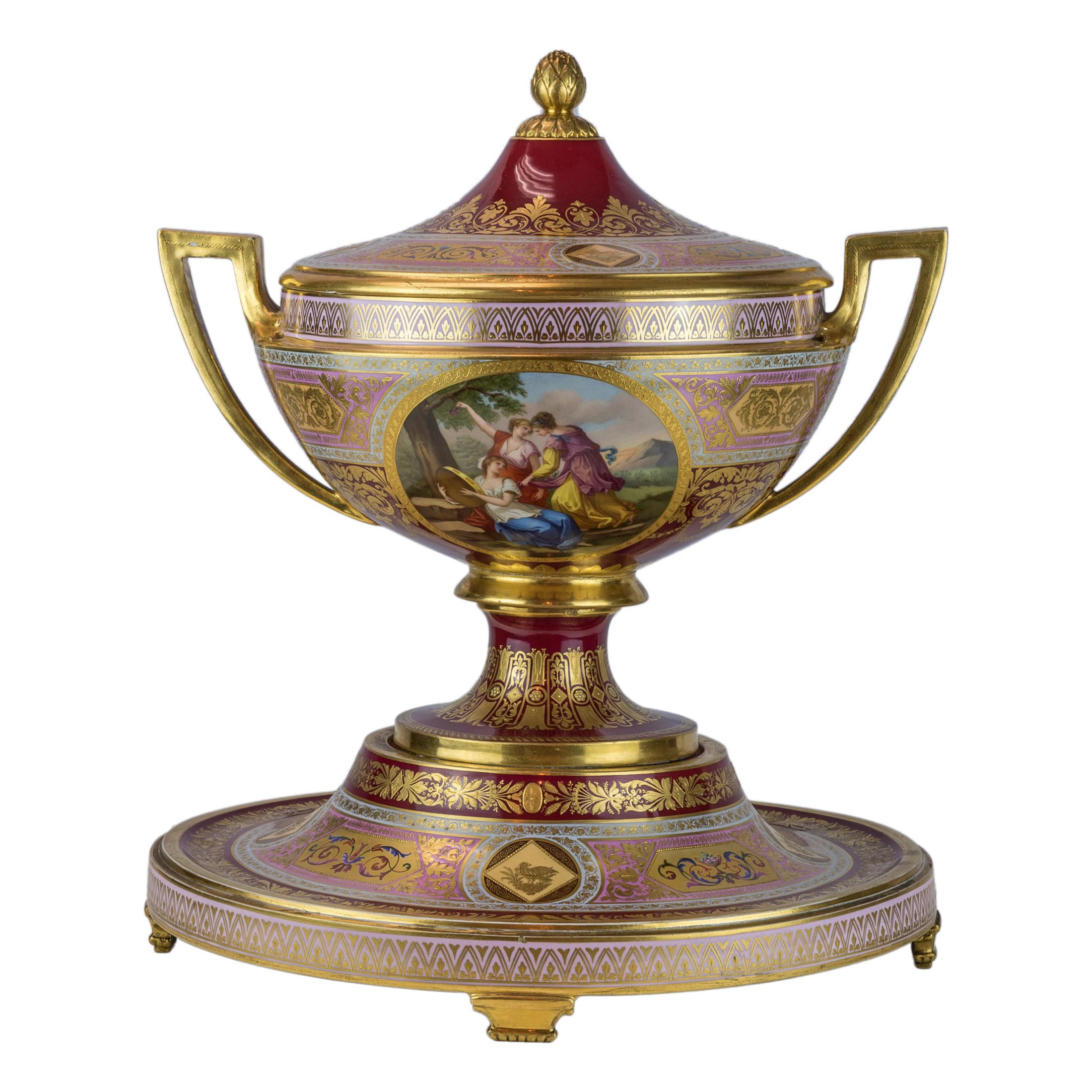 A fine Royal Vienna ruby red and pink porcelain covered centrepiece and stand
Scenic decorated three section centrepiece with a beehive mark on the underside. 

Date: 20th century
Origin: Austria
Size: 18 in high x 15 3/4 in wide (base); 10 1/2