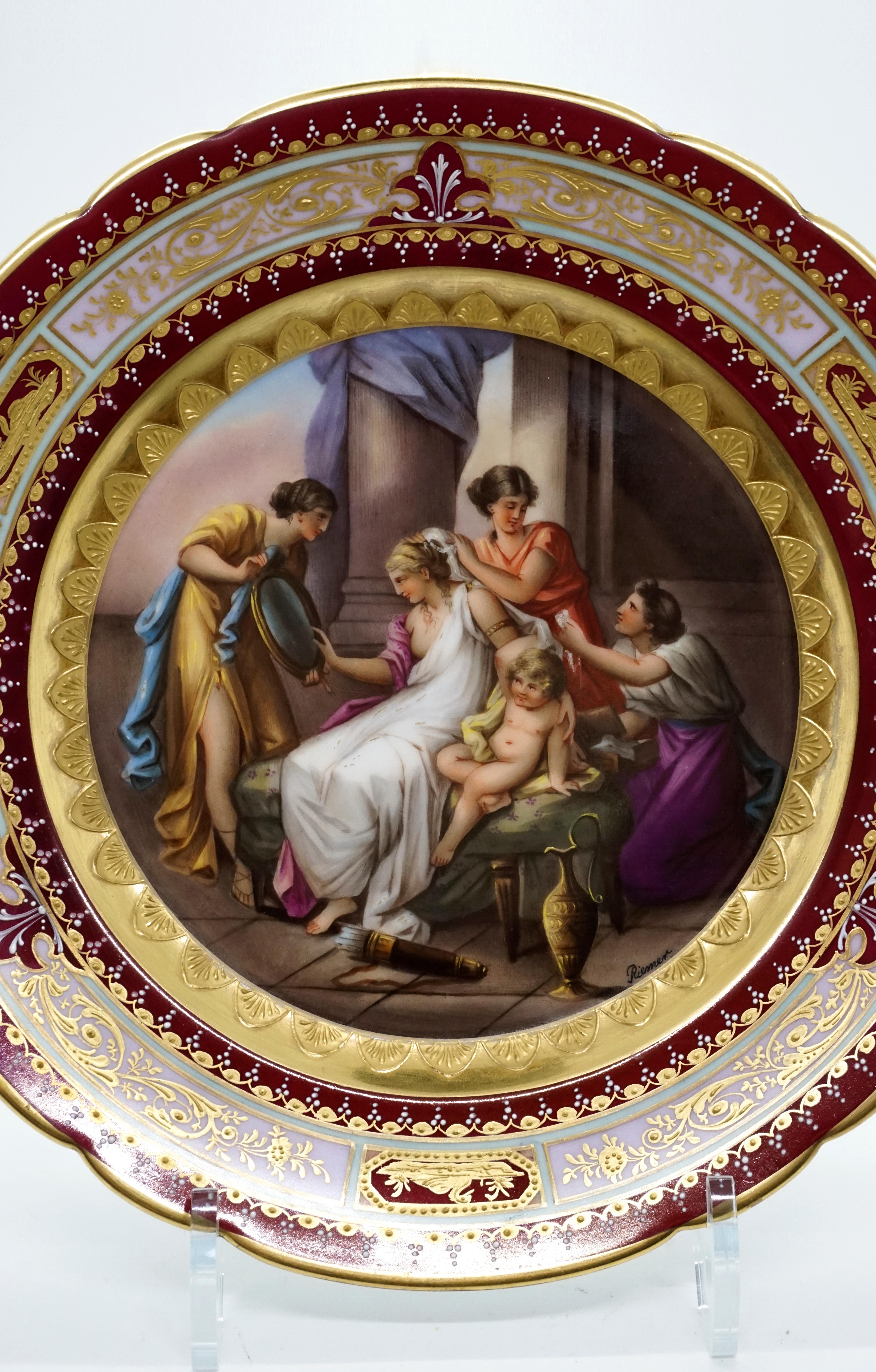 Elaborately painted porcelain picture plate: plate rim with notches, gold rim on the outside, ruby red flag, gold and white framed light green ribbon with three large, gold framed reserves with a pink background, filled with gold feather tendrils