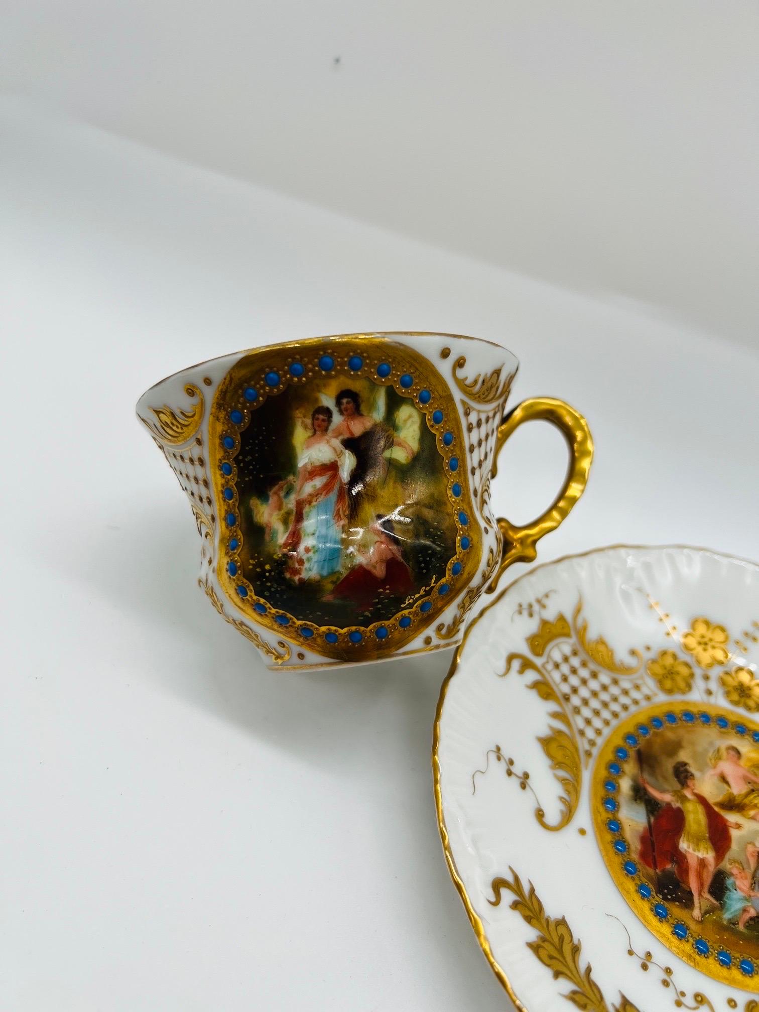 Royal Vienna Style Hand Painted Porcelain Teacup & Saucer. 
The cup and saucer are heavily decorated with raised enamel and gilding across the surface and showcase a scene of 3 ladies. Interior heavily gilt. Underside marked.