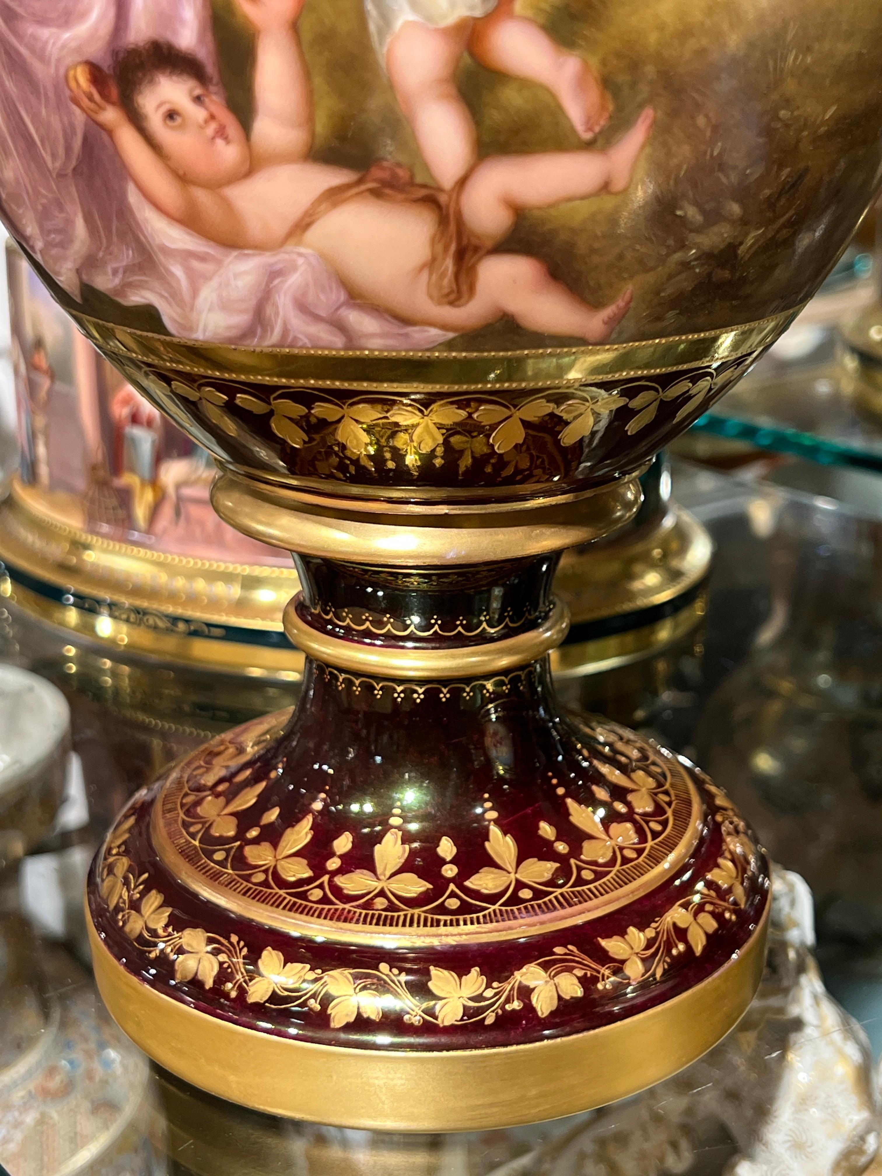 Royal Vienna style porcelain vase with with extensive gilt decorations over a burgundy red glazed ground, featuring a painted scene of a mother and children gathering flowers, wheat and other bounty, symbolic of autumn, and a wooded meadow on