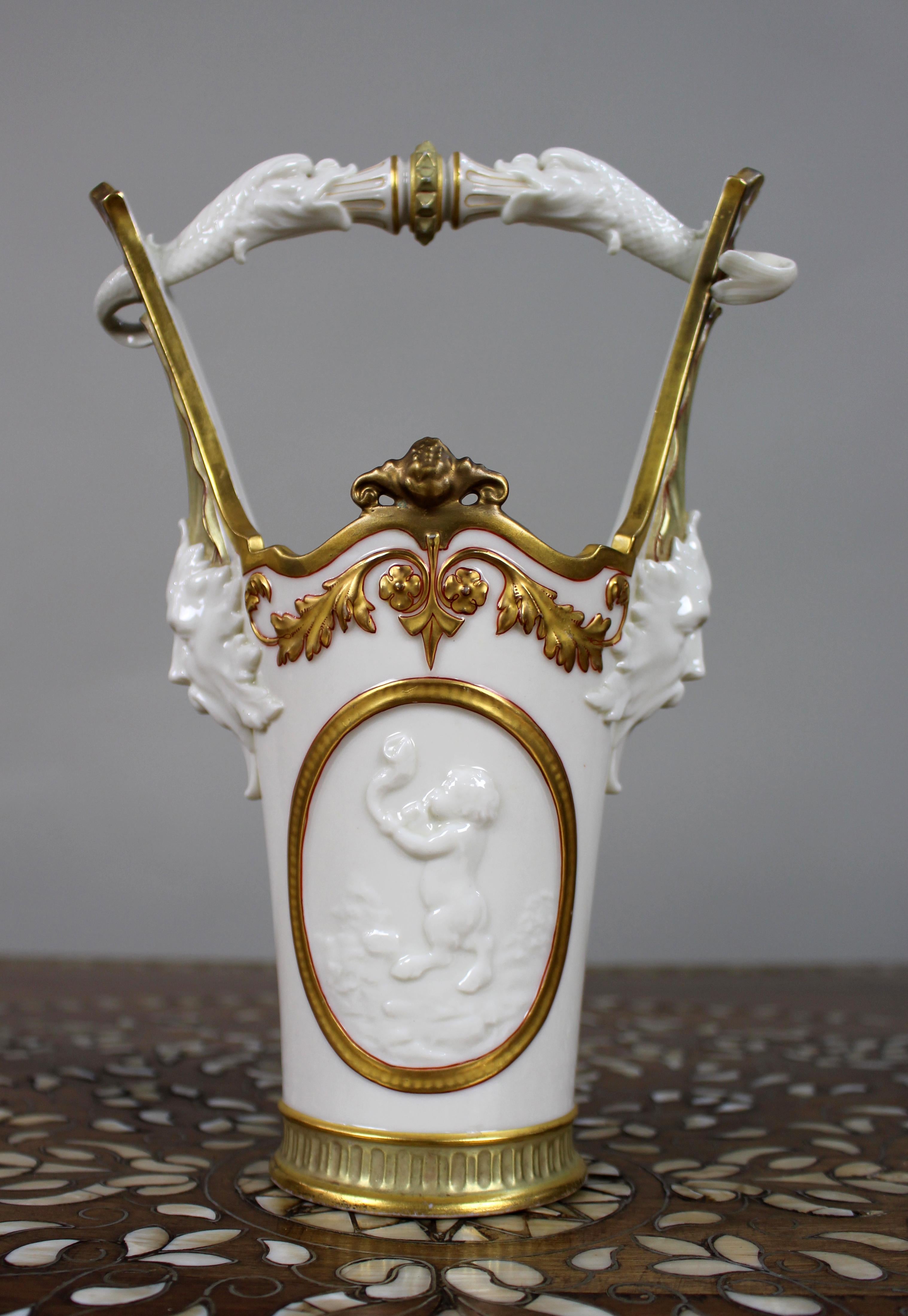 Royal Worcester Exhibition Vase with Dolphin Handle, Mask Heads & Cherubs – 1884
An exceptional Royal Worcester porcelain exhibition vase, dated 1884, retailed by the distinguished firm A.B. Daniell & Son of Wigmore Street, London. This rare and