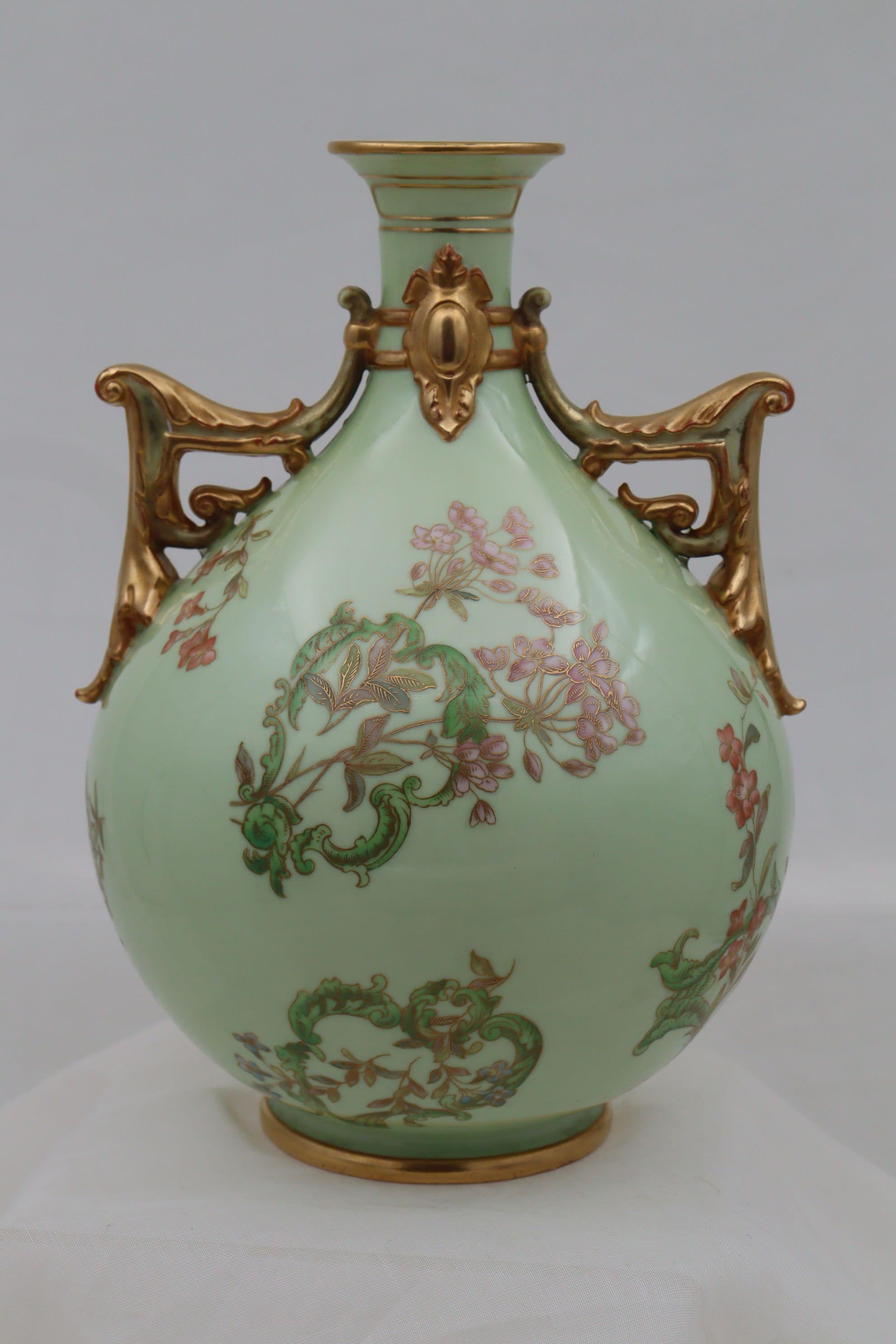 Ce vase à deux anses en porcelaine globulaire de Royal Worcester présente un décor inhabituel, peint à la main et doré, qui comprend une série de cartouches de forme irrégulière formés par des feuillages stylisés, à travers lesquels sont enfilées