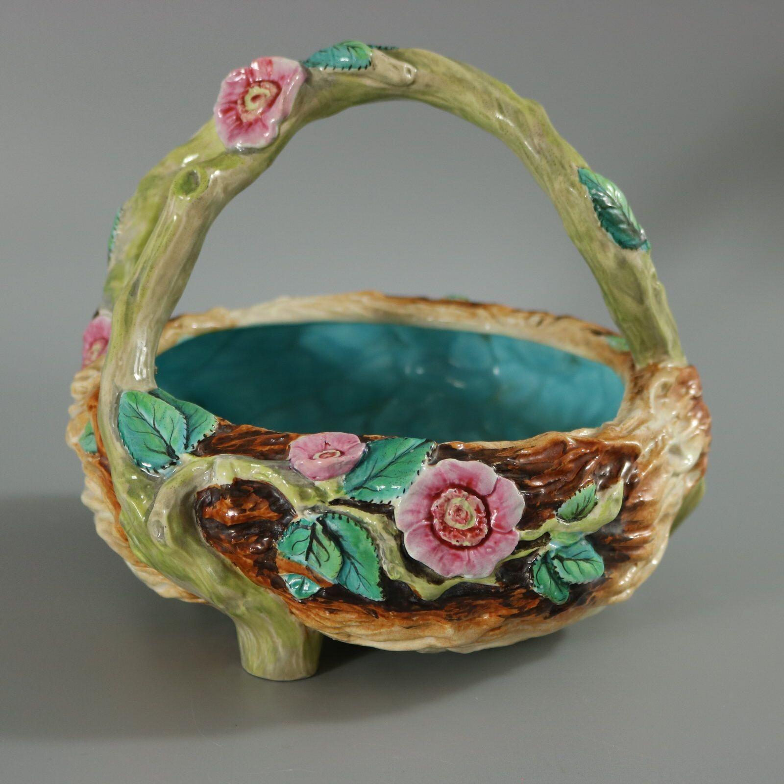 Royal Worcester Majolica basket which features pink flowers and green leaves, which are hand painted and overglazed. Green branch molded handle and three feet. Colouration: green, pink, brown, are predominant. The piece bears maker's marks for the
