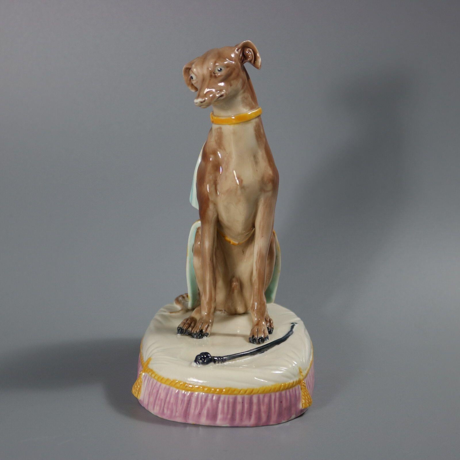 Figura in maiolica di Royal Worcester che raffigura un levriero seduto su un cuscino, con una coperta sulla schiena. Colorazione: predominano il rosa, il marrone e il bianco. Il pezzo reca un marchio di fabbrica dipinto.