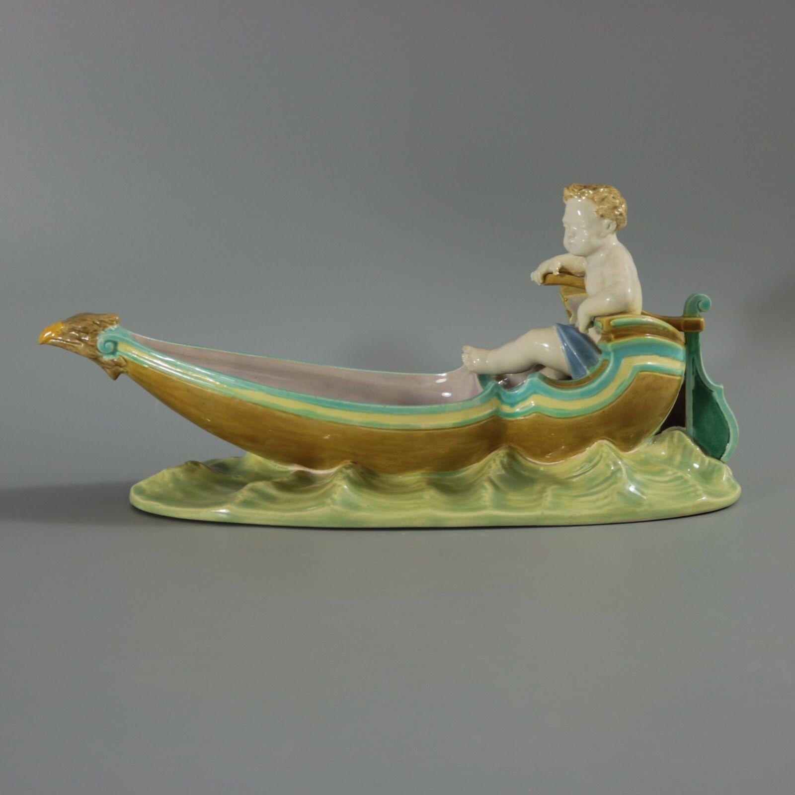 Royal Worcester Majolica figural dish which features a putto seated on a gondola boat, with an eagle figurehead. Colouration: turquoise, white, brown, are predominant. The piece bears maker's marks for the Royal Worcester pottery.