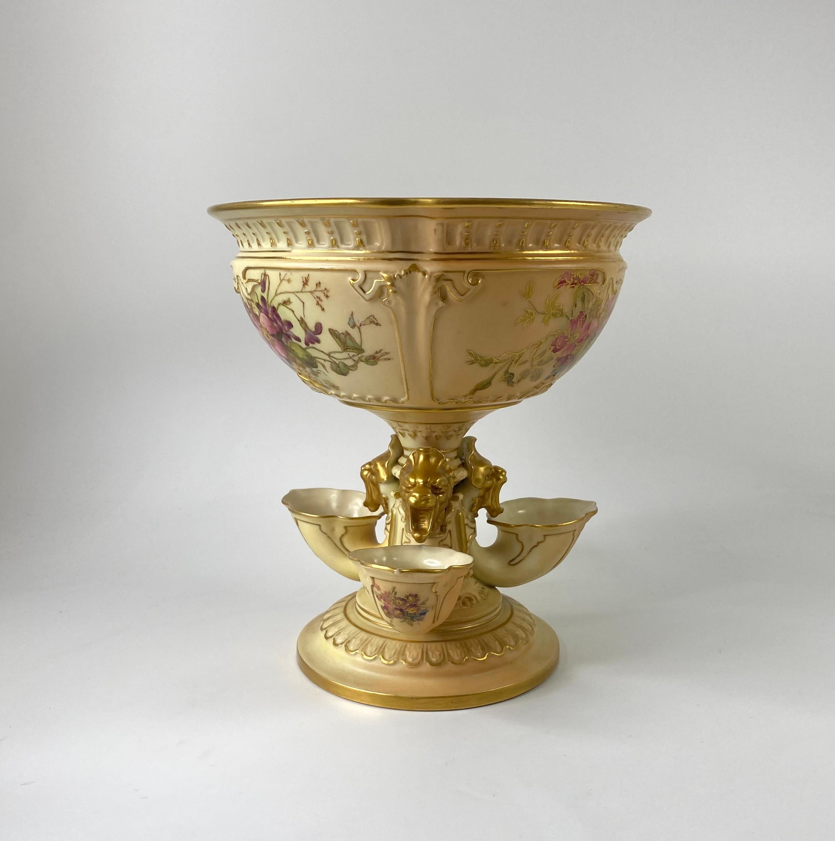 A large Royal Worcester porcelain ‘Flower Bowl’, dated 1912. The ‘Blush ivory’ decorated bowl modelled in Renaissance style, as a large bowl set upon a pedestal, with three gilt decorated grotesque masks, over three cornucopia, above a moulded