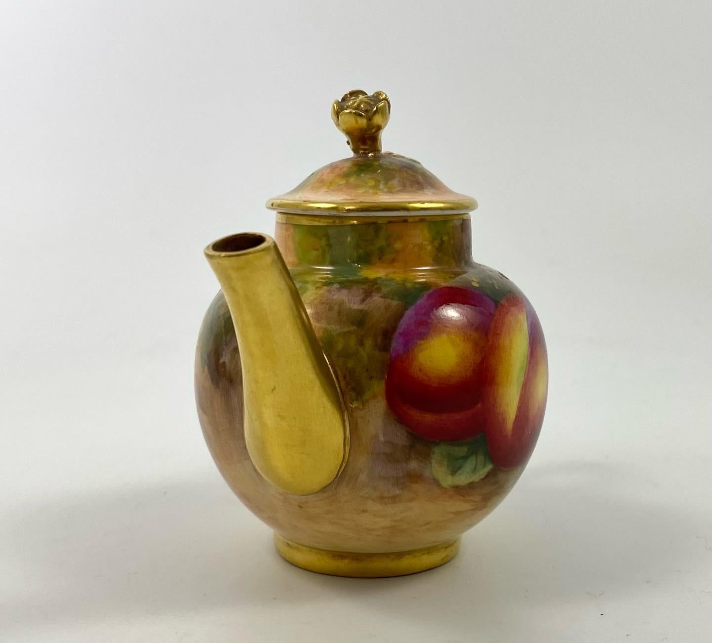 Royal Worcester miniature porcelain teapot, dated 1953. The globular teapot, finely painted by Harry Ayrton, with a study of fruit, on a mossy bank. Having a gilded spout, and handle.
The cover similarly decorated, and surmounted with a gilt floral