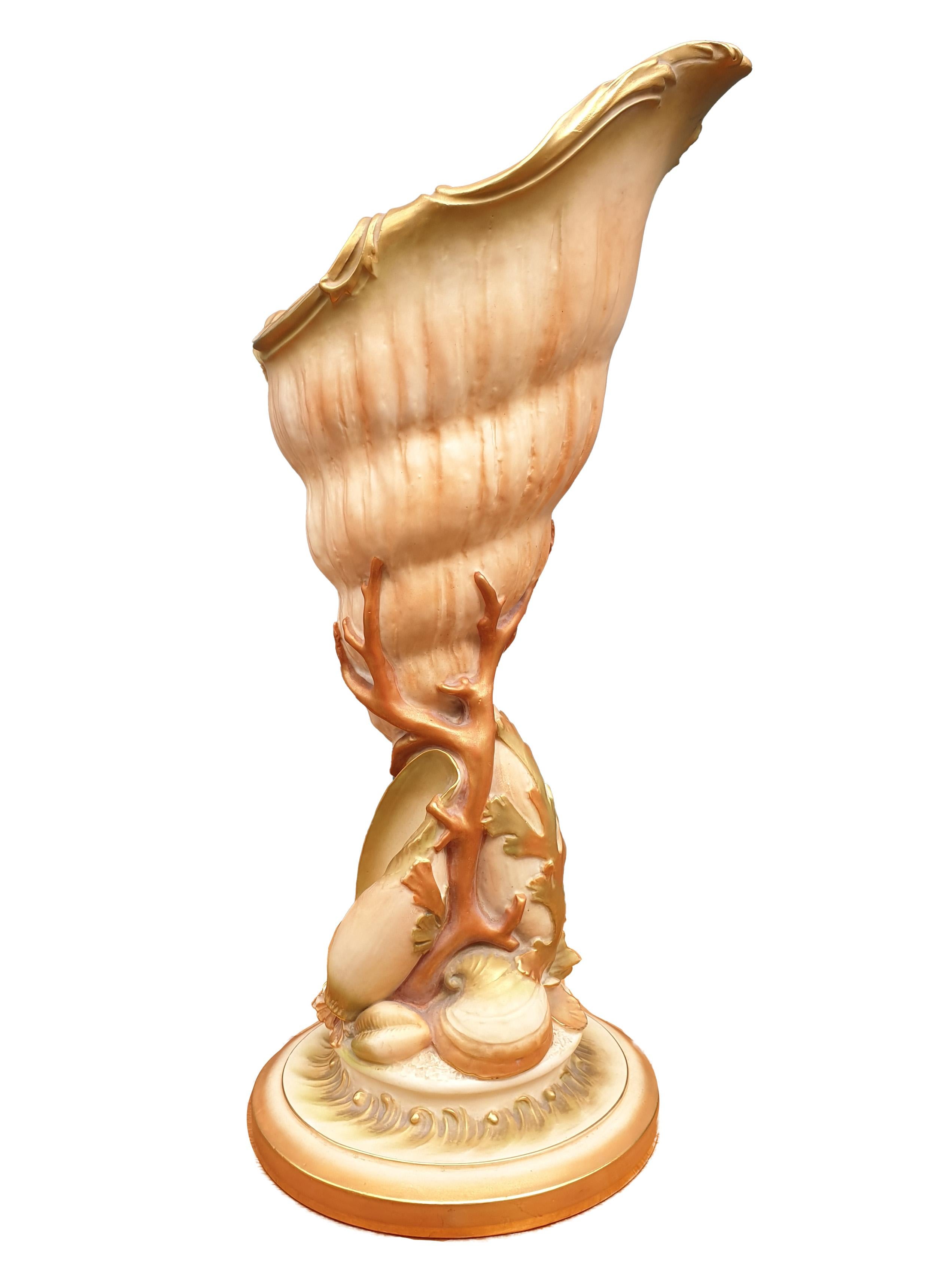 An impressive Royal Worcester Shell Vase, c. 1903, modeled in shape of a large shell with smaller shells leaves and pieces of corals adorning the base finished in blush ivory and gilt. Standing upright and with a peak towards the side the edges at