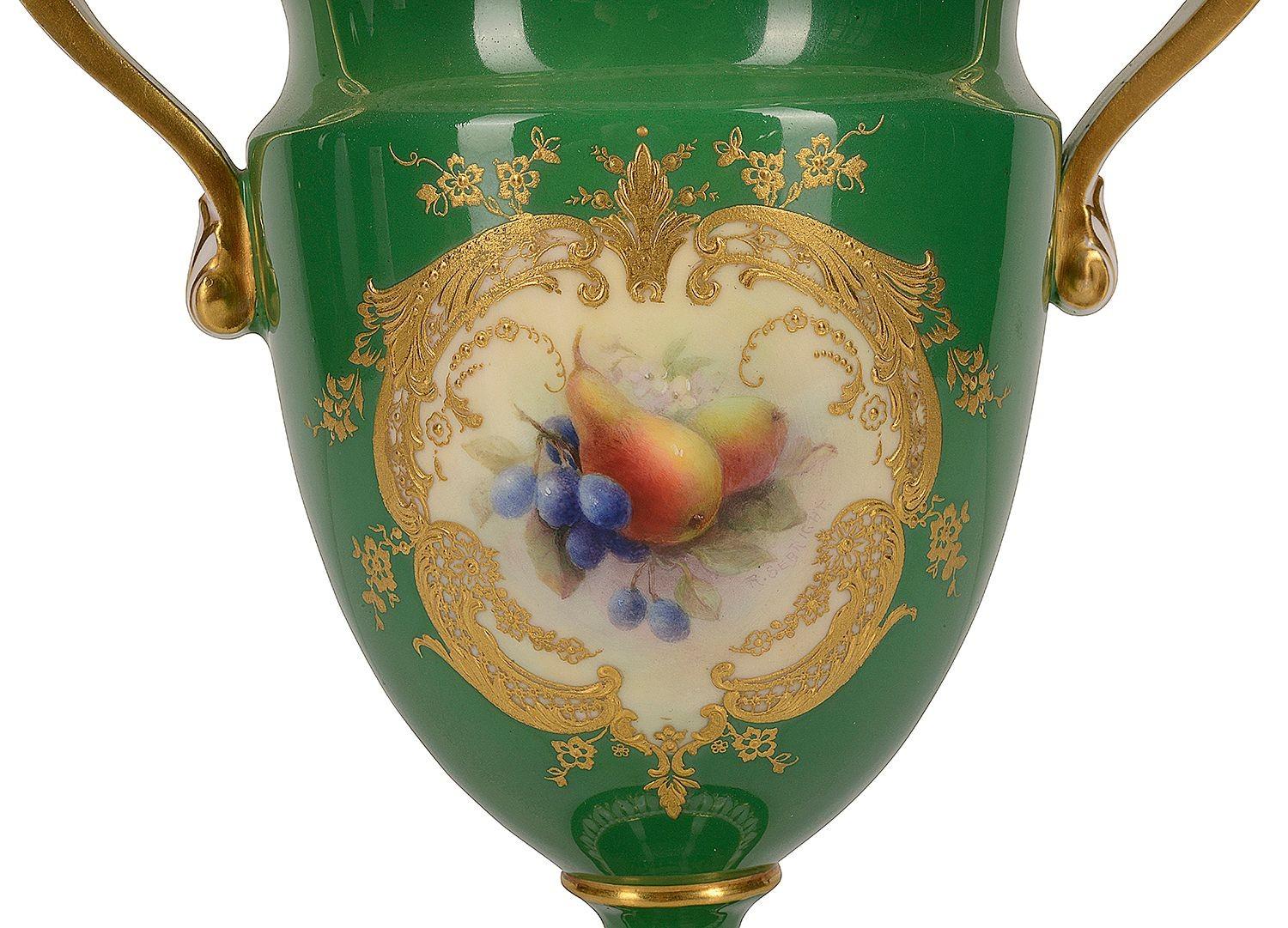 Vase à deux anses en porcelaine Royal Worcester de belle qualité, présentant un fond vert pâle avec des bordures et des éléments décoratifs classiques dorés, le panneau inséré peint à la main représentant des poires, des fleurs et des baies. Signé