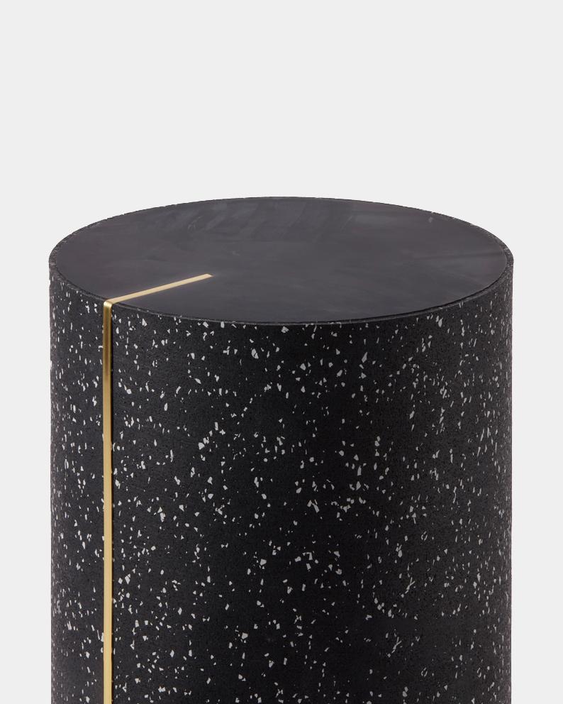 The Rubber CYL black concrete is a hand-cast concrete side table with a tinted black concrete top. The series of accent pieces brings together recycled rubber on the exterior, cast together with concrete and a brass inlay. 

The exterior of the