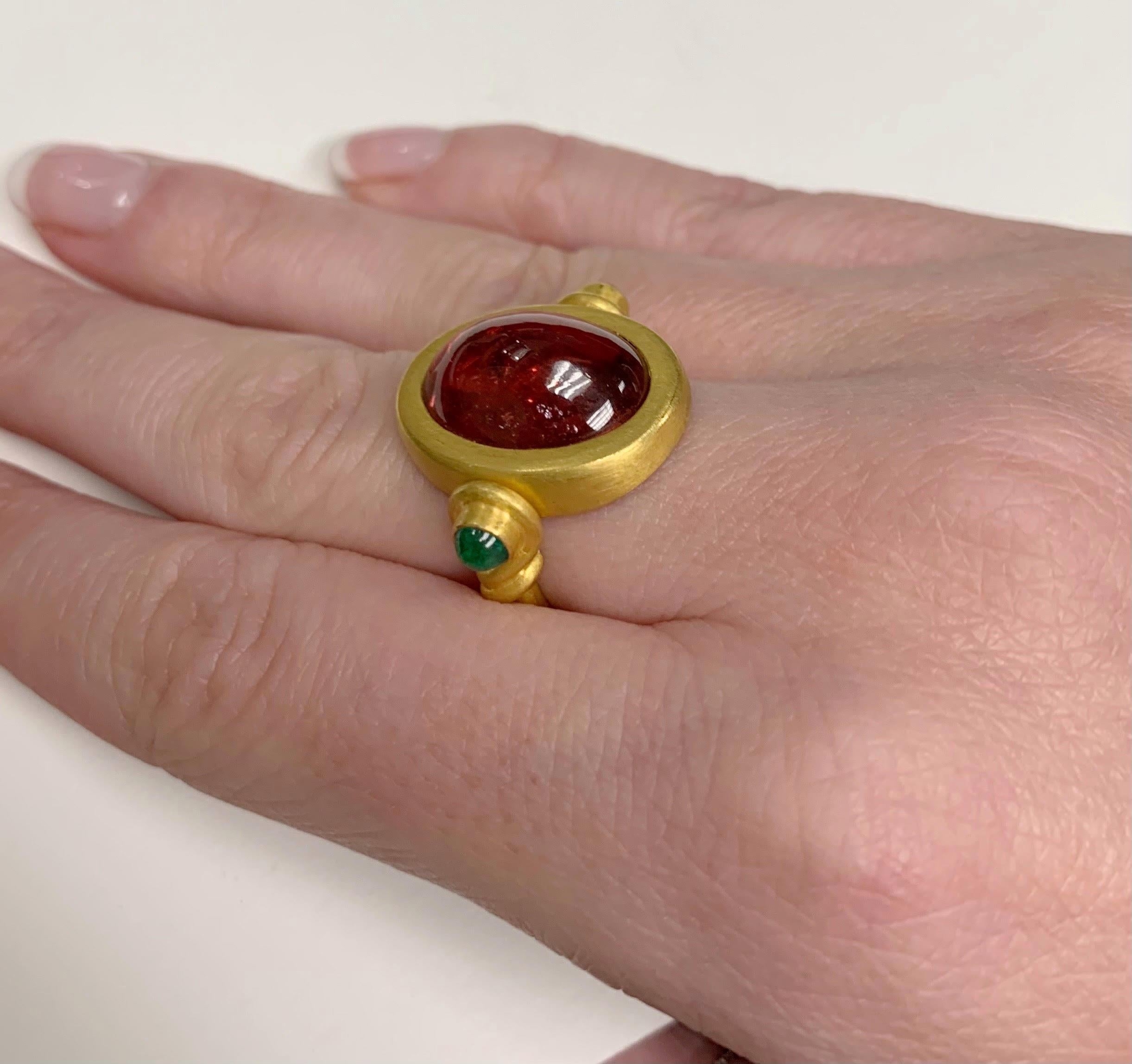 This playful cocktail ring is made of 22 karat yellow gold and features a large cabochon cut Rubelite Tourmaline. 2 Emerald cabochons are set on the top of the band. The center stone swivels independently from the ring as a design feature. The
