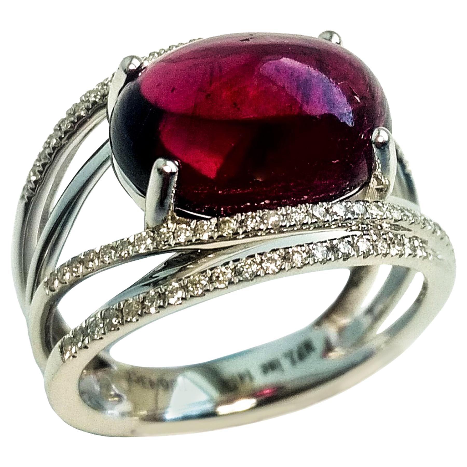 Contemporary, unique design, deep red cabochon rubellite, set in high profile mount with 4 prongs. Oval translucent, glassy looking rubellite, accented with sparkling round brilliant cut diamond design. Handcrafted in 14 karat white gold. 

The