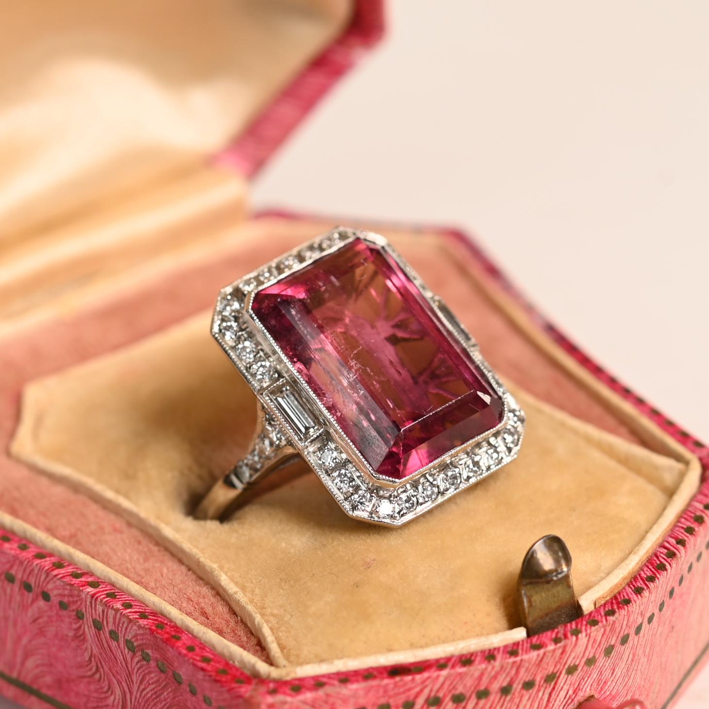 Cette bague exquise présente en son centre une rubellite de taille émeraude d'environ 12,10 carats, qui rayonne d'une teinte riche et vibrante. La rubellite est entourée d'un halo lumineux de diamants de taille européenne ancienne, méticuleusement