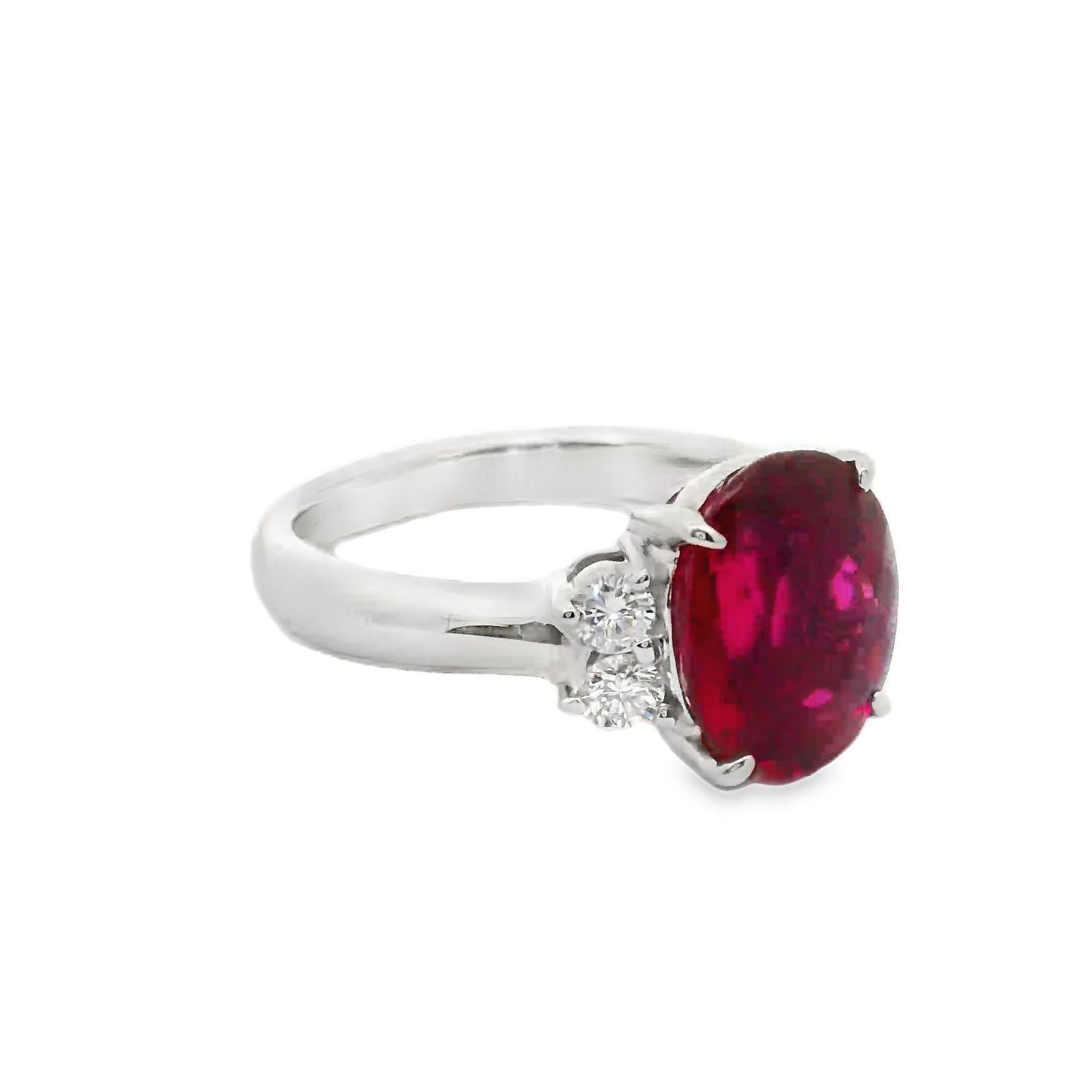 A contemporary ring featuring a 3.2 carat rubellite with an oval cut. The rubellite displays a vivid red color, exuding depth and intensity. It is flanked by 0.27 carats of round-cut diamonds, which add a touch of brilliance with their white