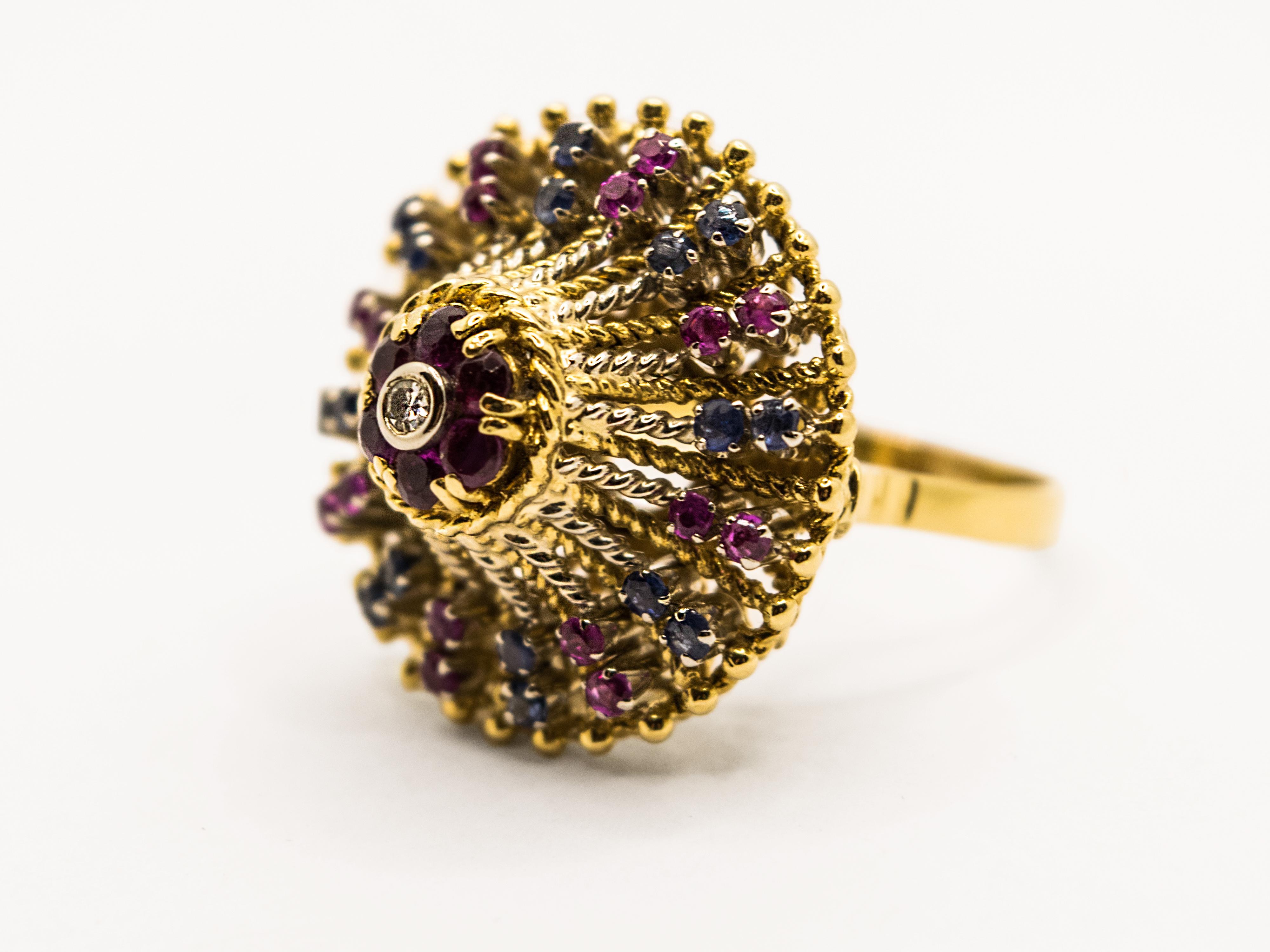 Vintage cocktail ring ( circa 1950s to 1960s ) set with a cluster of blue sapphires and rubies in a high rising dome mount and one diamond at the top.
Crafted in 18 Kt yellow gold with a romantic woven pattern.
This ring is in excellent original