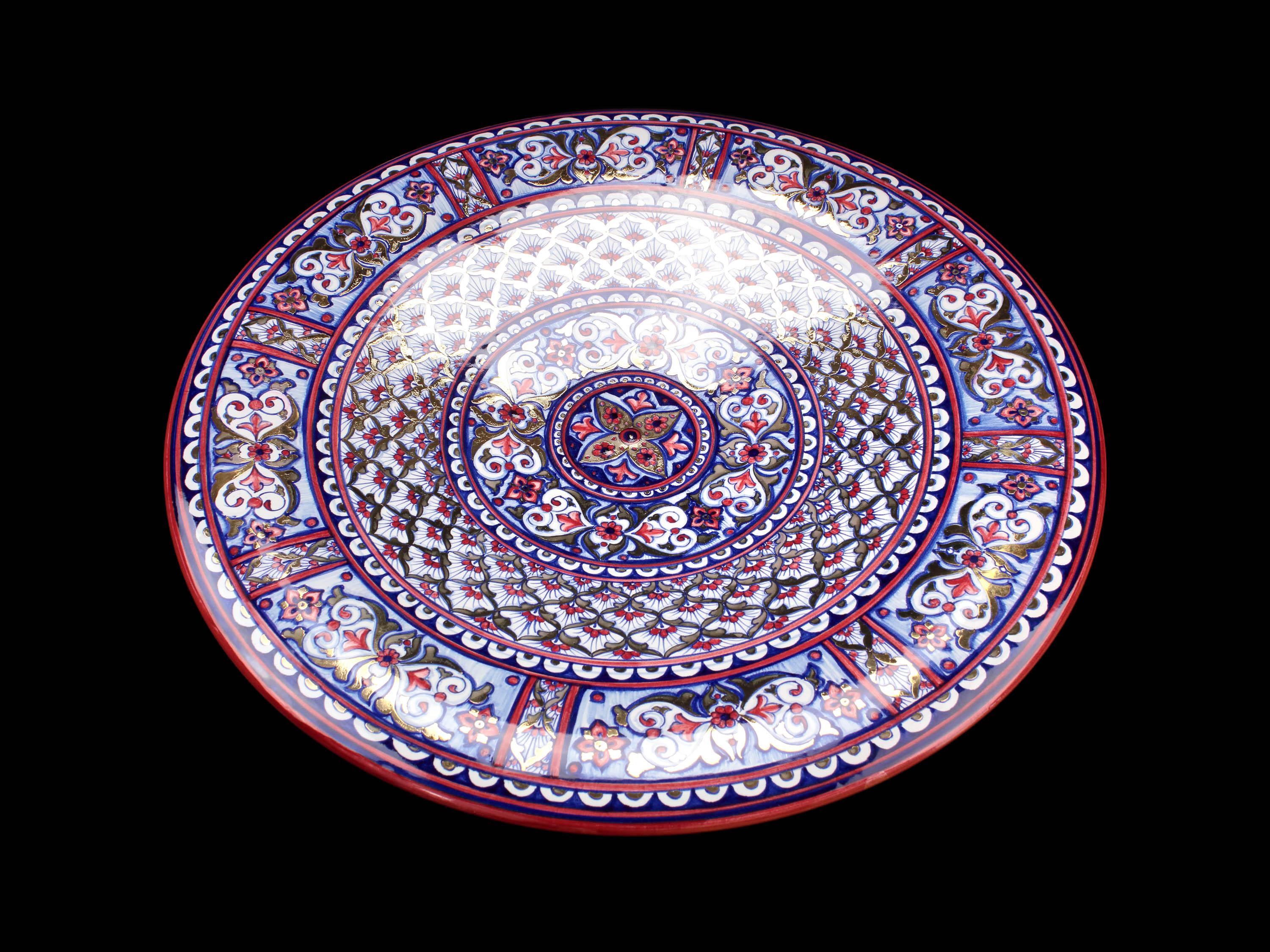 The dish, made of majolica painted in duotone of blue and red, features dense decoration, inspired by the Moorish style, throughout its surface. The outer band of the brim is richly embellished with spiral plant ornaments that are repeated in mirror