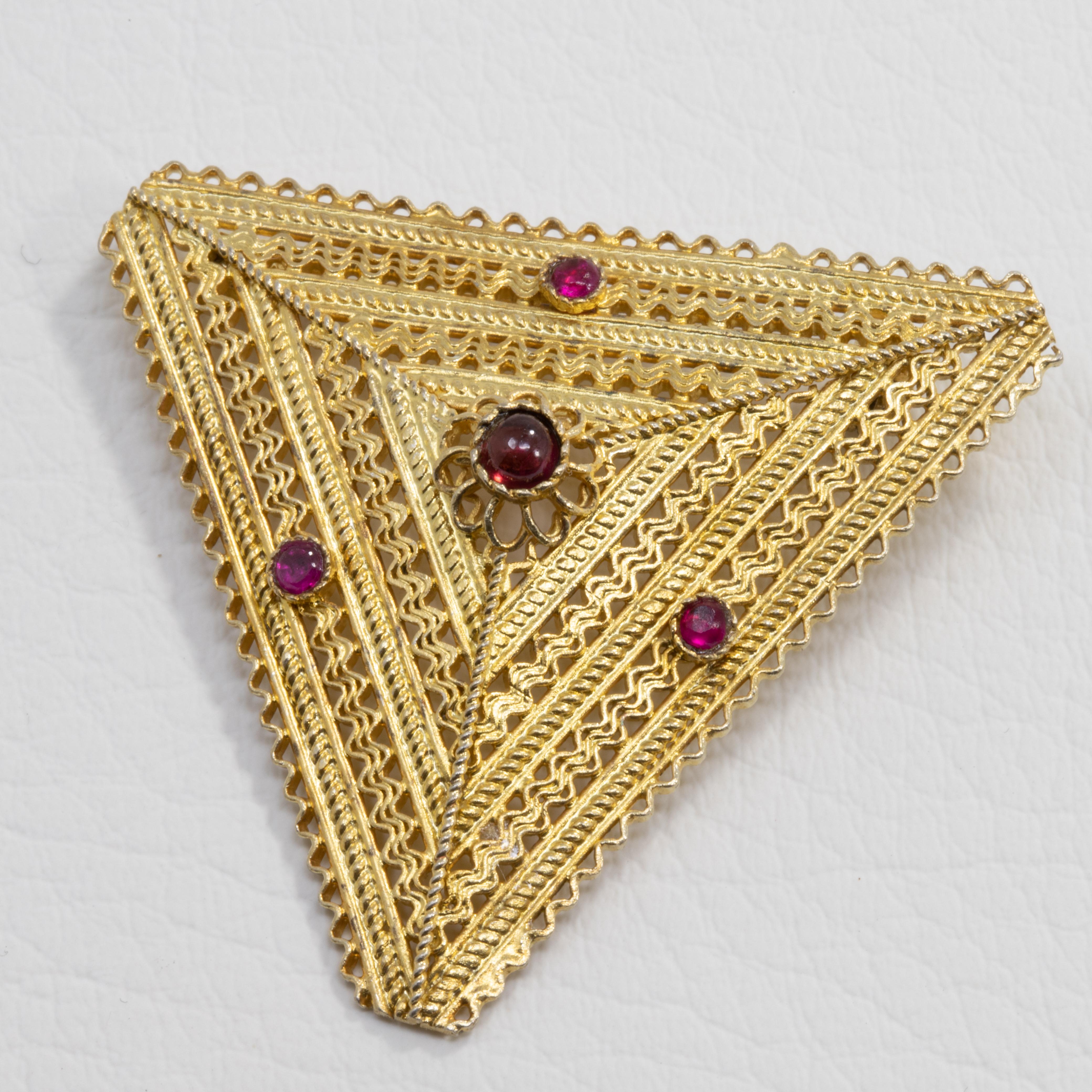 An exquisite brooch! Features a triangular, intricately accented, gold-plated metal setting with a centerpiece amethyst cabochon, which resembles a floral motif. Three faceted rubies, 2.3mm in diameter, are set around the center motif.

Light wear