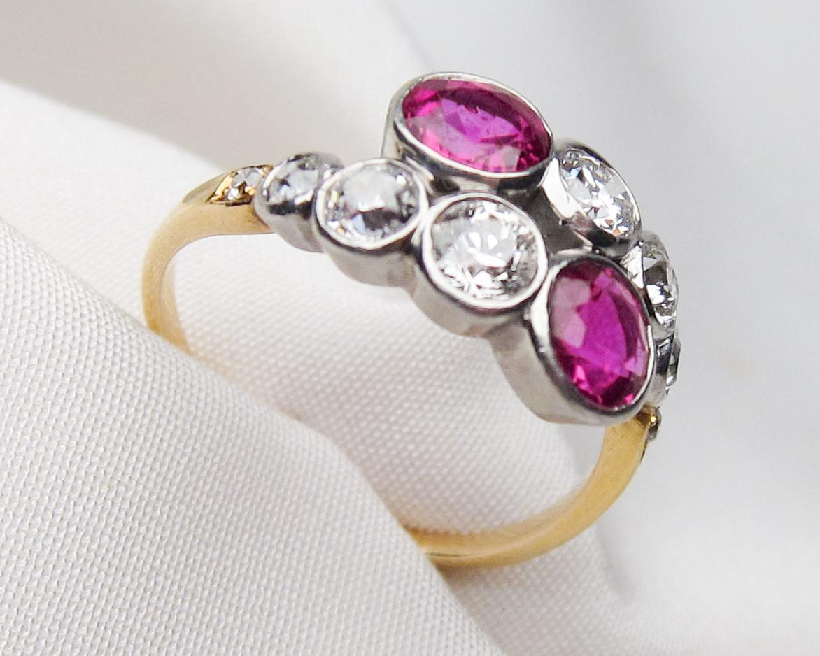 Circa 1900. This lovely platinum-topped 18KT yellow gold late Victorian bypass ring features two bezel-set round mixed-cut natural purplish-red rubies weighing 1.40 carats total. Accenting the rubies are six bezel-set old European-cut diamonds and