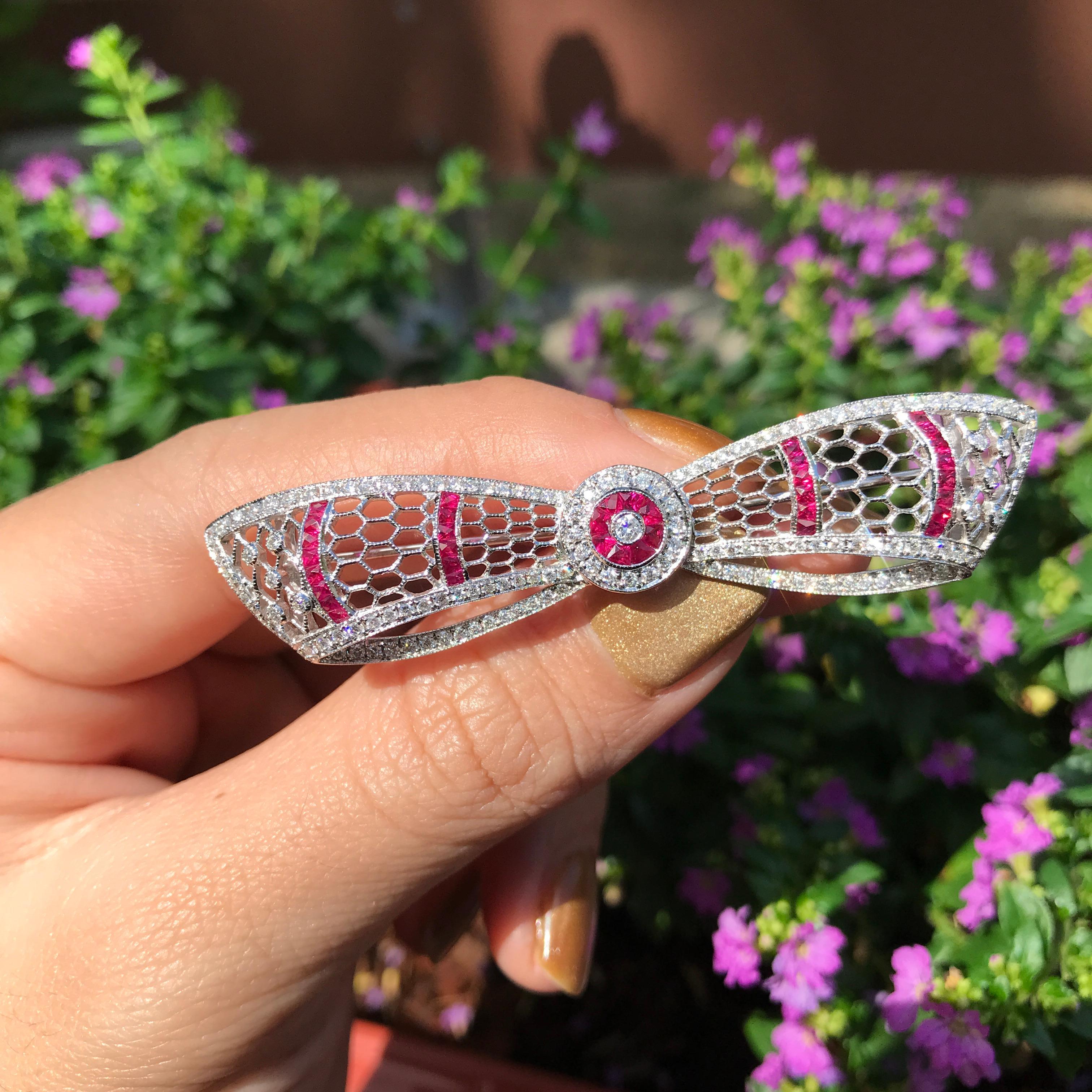 An elegant Art Deco-style bow brooch adorned with dazzling rubies and diamonds. The intricate bow design is highlighted by the sparkling contrast of the gems .Diamonds grace the curves, while rubies add a rich, vibrant pop of color. A timeless