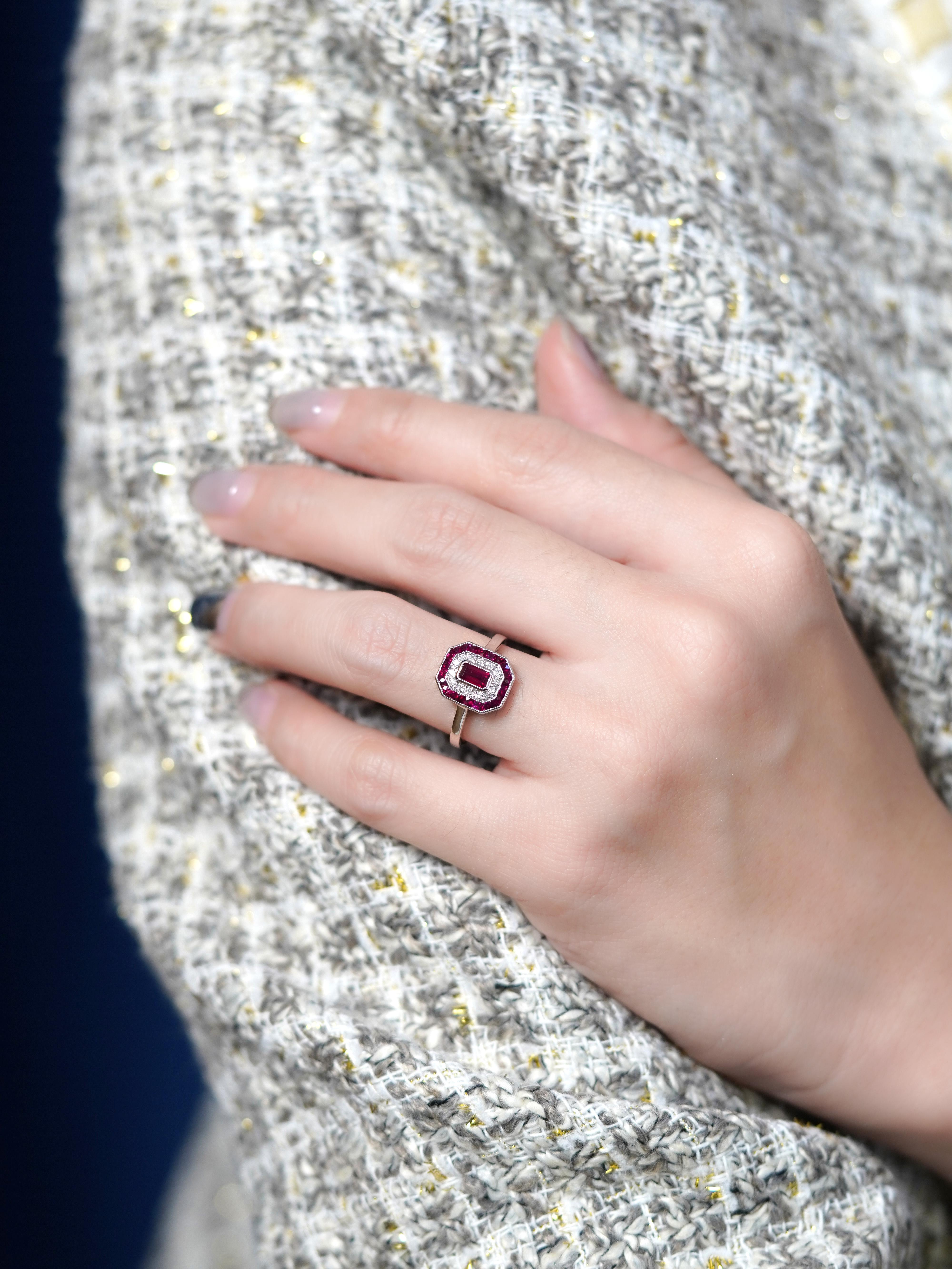 Bold color meets vintage glamour in this striking Art Deco-style engagement ring. At its heart, a vivid ruby glows with passion, surrounded by a sparkling halo of diamonds that add timeless brilliance. Framed with precision-set French-cut emeralds,