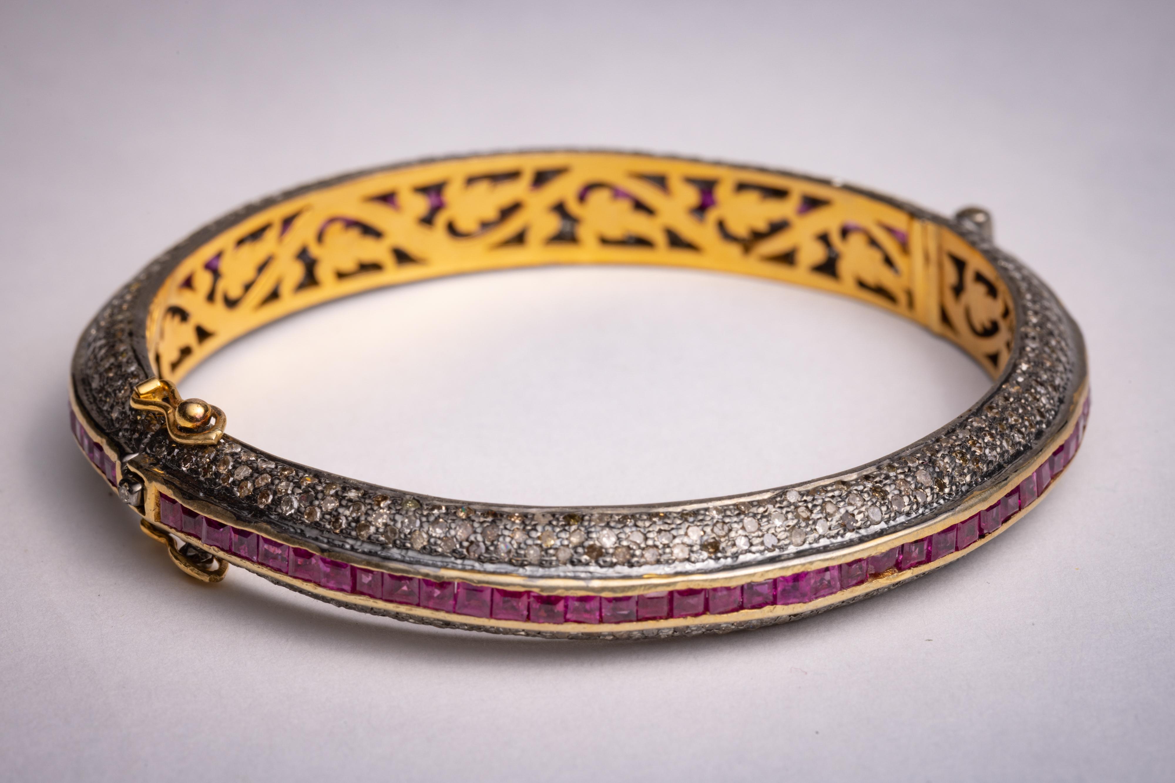 A ruby and diamond bangle with clasp.  Faceted square, channel-set rubies surrounded by round, brilliant cut diamonds in a pave` setting.  Stones are set in sterling silver and bracelet is lined in 18K gold.  Inside circumference is 7