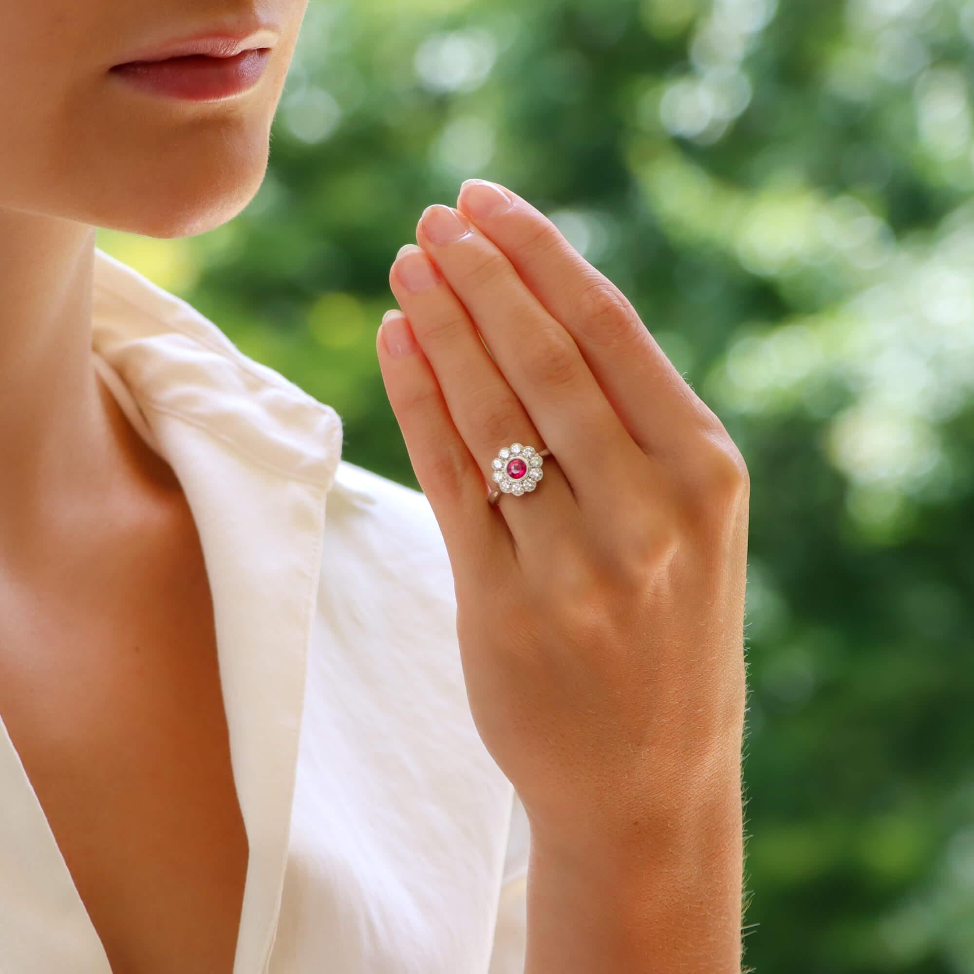 A beautiful ruby and diamond engagement/cocktail cluster ring set in 18k white gold. 

The ring is predominantly set with a vibrant round cut pinkish ruby which is rub-over set to centre. Surrounding the ruby is then a cluster of ten sparkly round