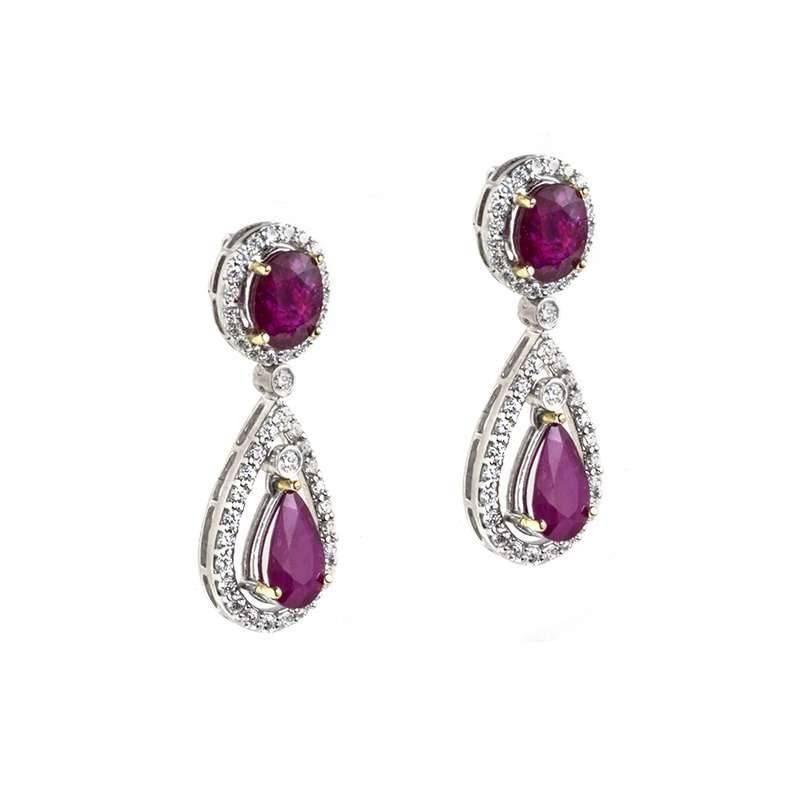 A pair of 18k white gold ruby and diamond earrings. Each earring is composed of an oval cut ruby set within a round brilliant cut diamond halo surround, with a pear shape drop, made up of an pear cut ruby and round brilliant cut diamond surmount.