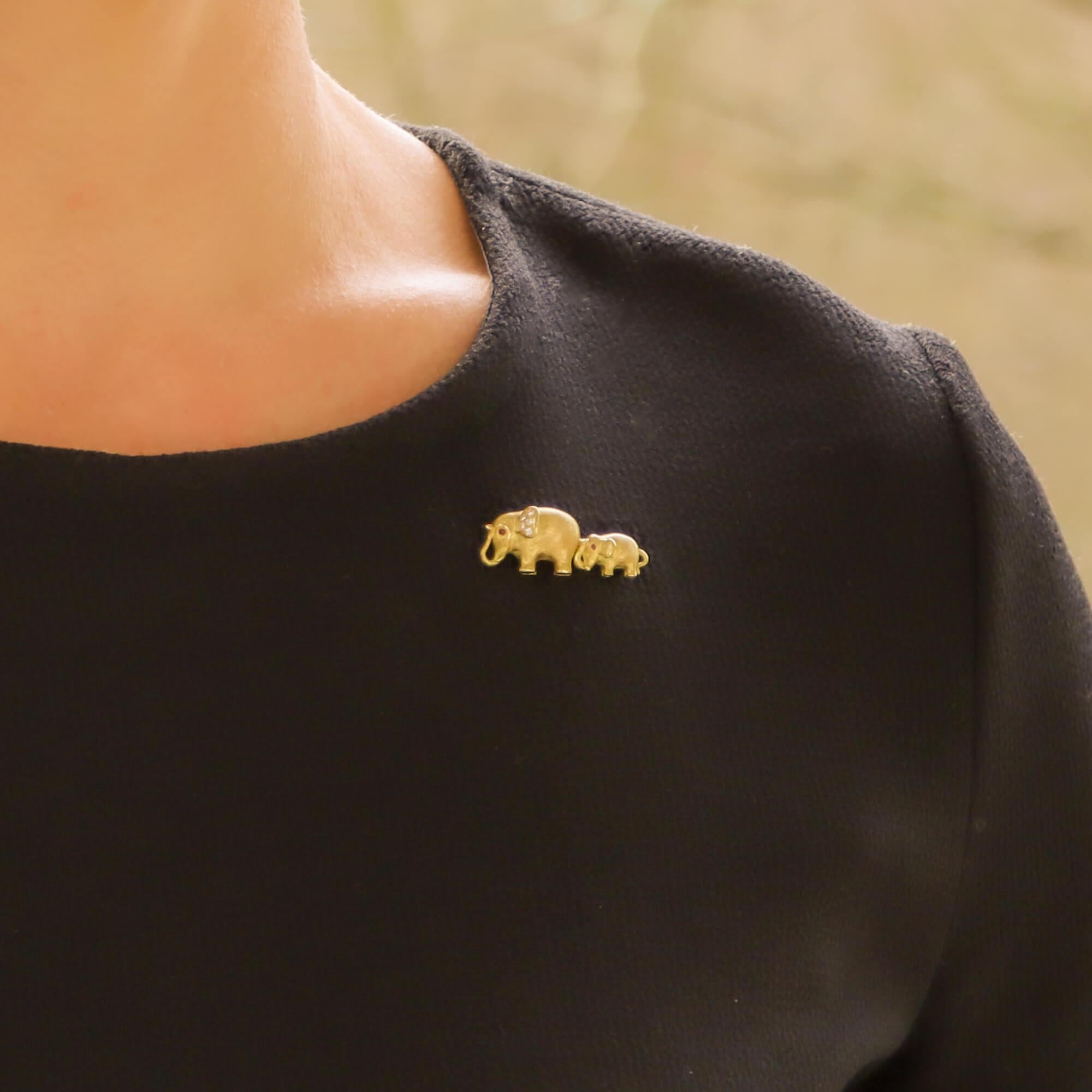 A lovely ruby and diamond Mother and baby elephant brooch set in 18k yellow gold.

The brooch depicts a mother and baby elephant connected to one another by tail and trunk. Both elephants are made of 18k yellow gold and have both been beautifully