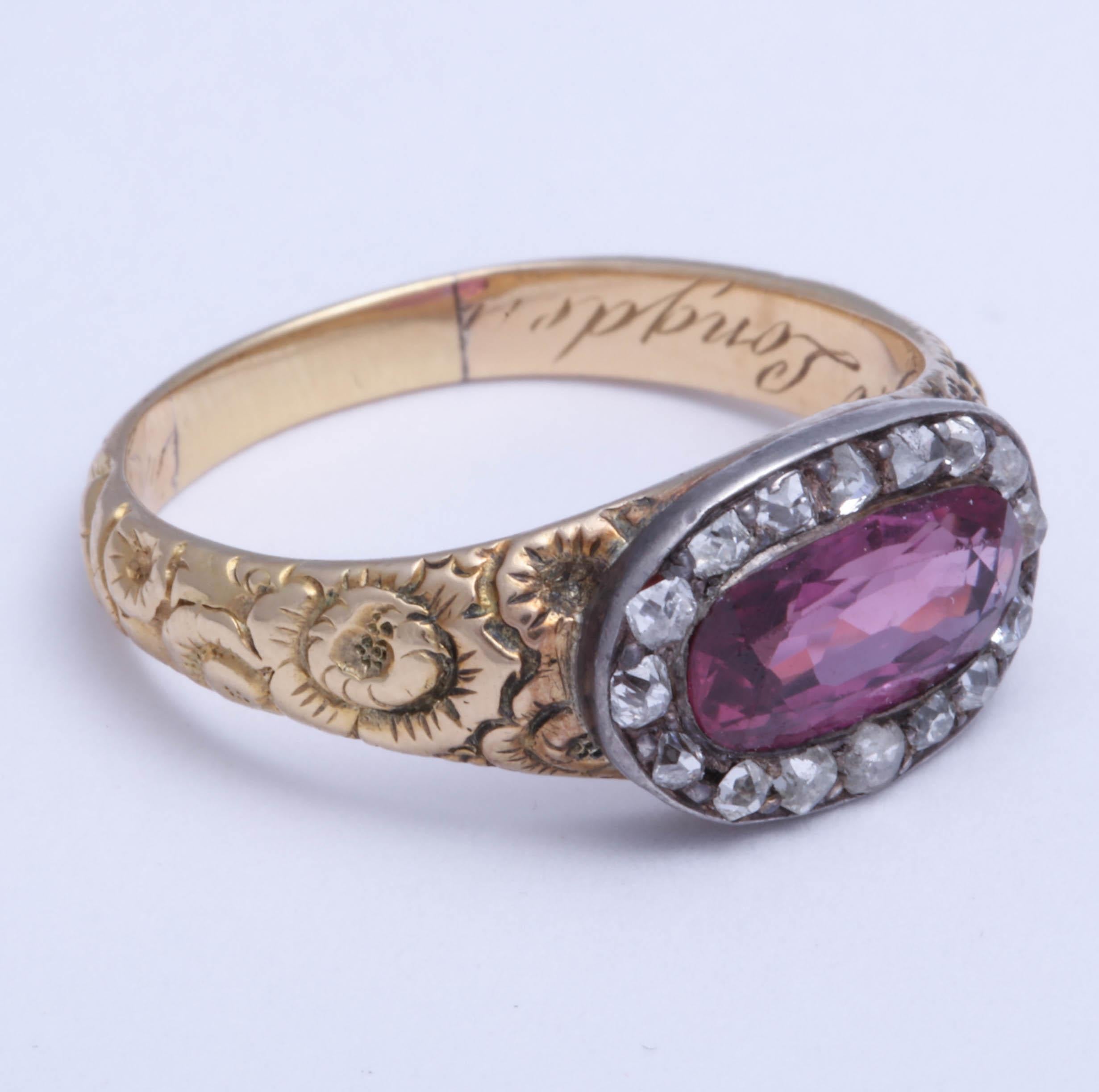 Lovely Georgian diamond ring with a large central faceted oval ruby set east to west surrounded by old cut diamonds. Beautiful floral engraving on the shank. Name and date engraved in the interior. Diamonds set in silver. Yellow gold is high karat. 