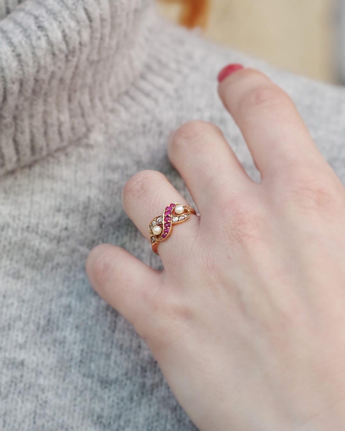 Antique infinity ruby diamond ring in 18 karat gold. The infinity motif (a horizontal figure 8) is set with seven natural round rubies, six rose-cut diamonds, and two fine pearls. The shoulders of the ring are adorned with small rose-cut diamonds.
