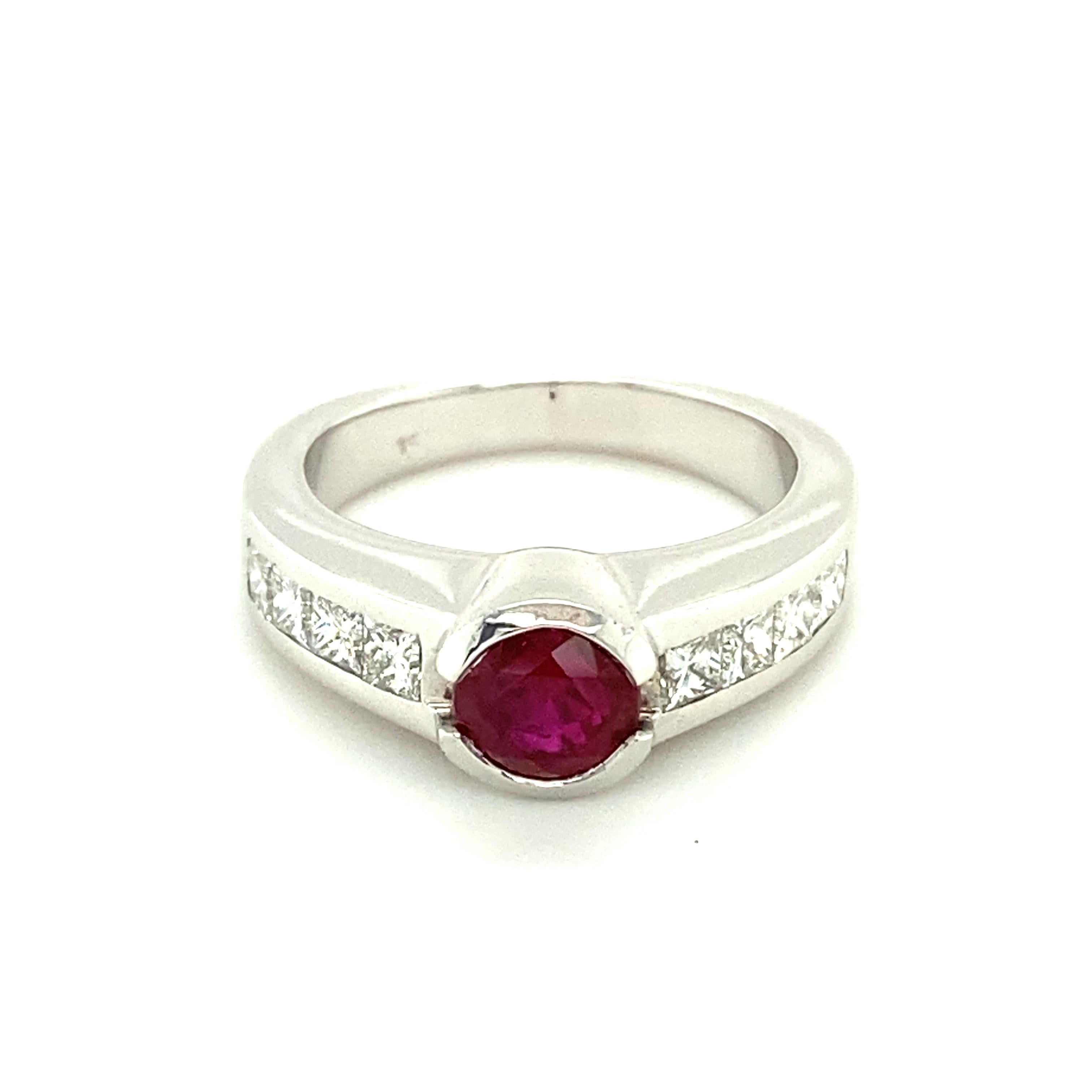 This beautiful ring in 18 karat white gold is set with a round facetted Burmese ruby of vivid colour, weighing approximately 1.27 carats. 
Set in a half-bezel, the lively ruby is accented by 8 channel set princess-cut diamonds of G/H colour and vs