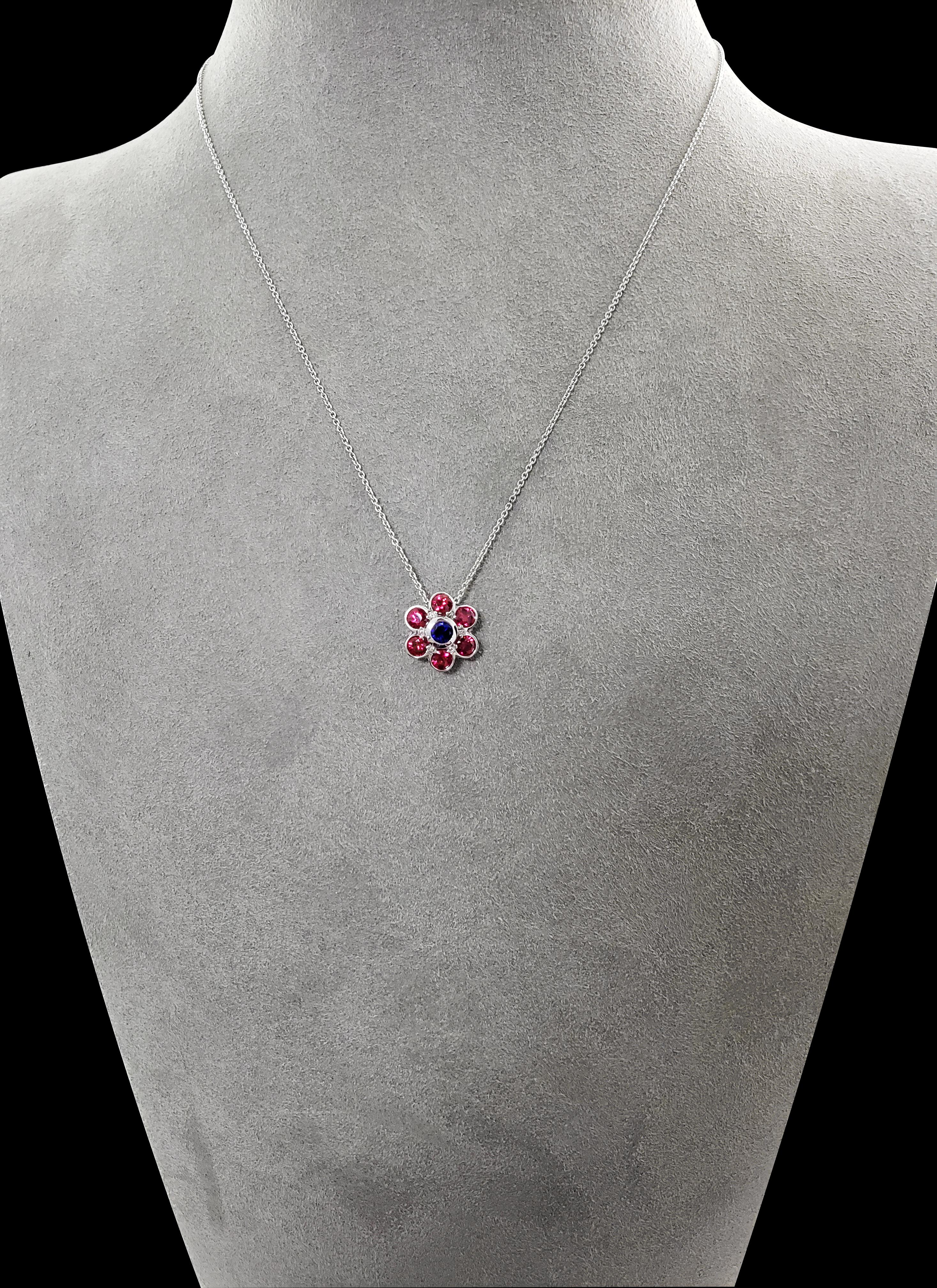 A colorful pendant necklace suitable for a casual and everyday wear. Features a 0.27 carat blue sapphire surrounded by 6 rubies (1.26 carats total) in a floral motif. Each gemstone is bezel set in 18 karat white gold. Attached to a 16 inch white