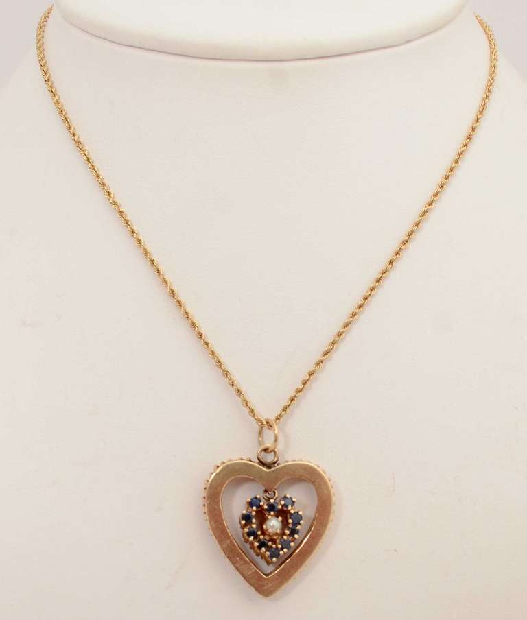 This pendant has three hearts in one. Within the outer gold heart is a ruby heart centered with a pearl. It reverses to a sapphire heart with pearl. The outer heart measures 1