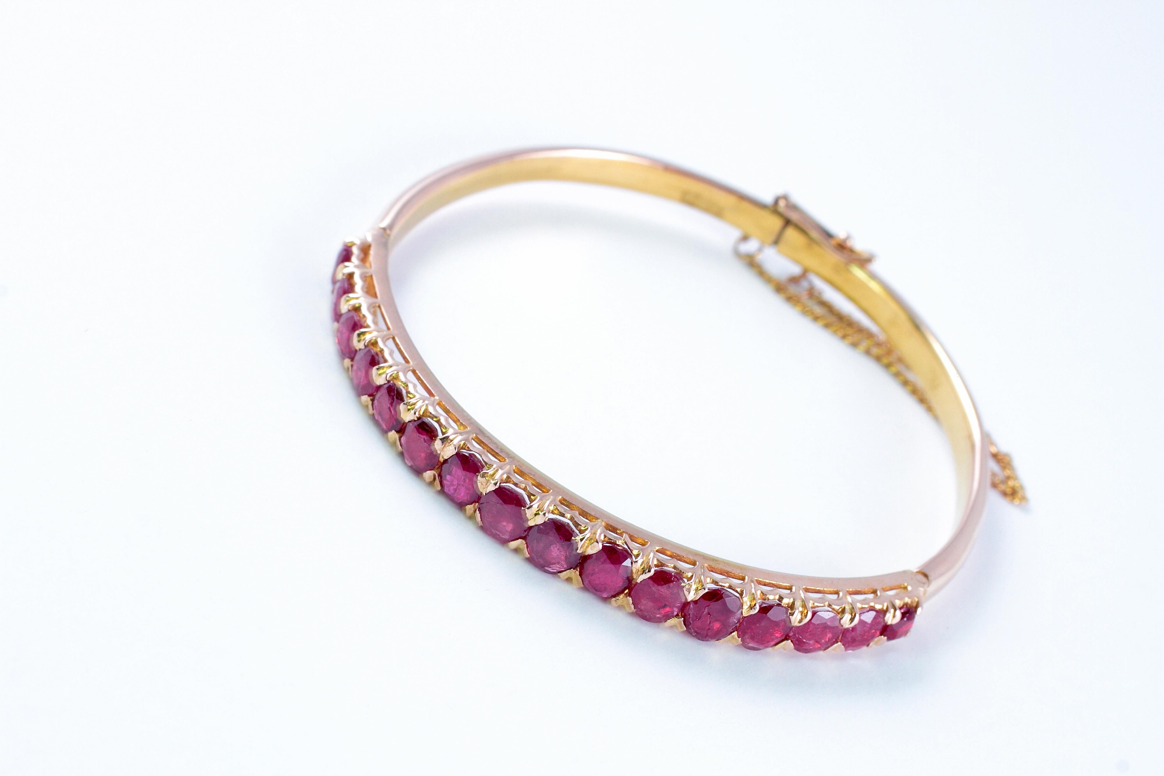 This timeless 14 karat yellow gold bangle features sixteen rubies across the top.  It opens to fit easily over the hand, and it is secured with both a clasp and safety chain.