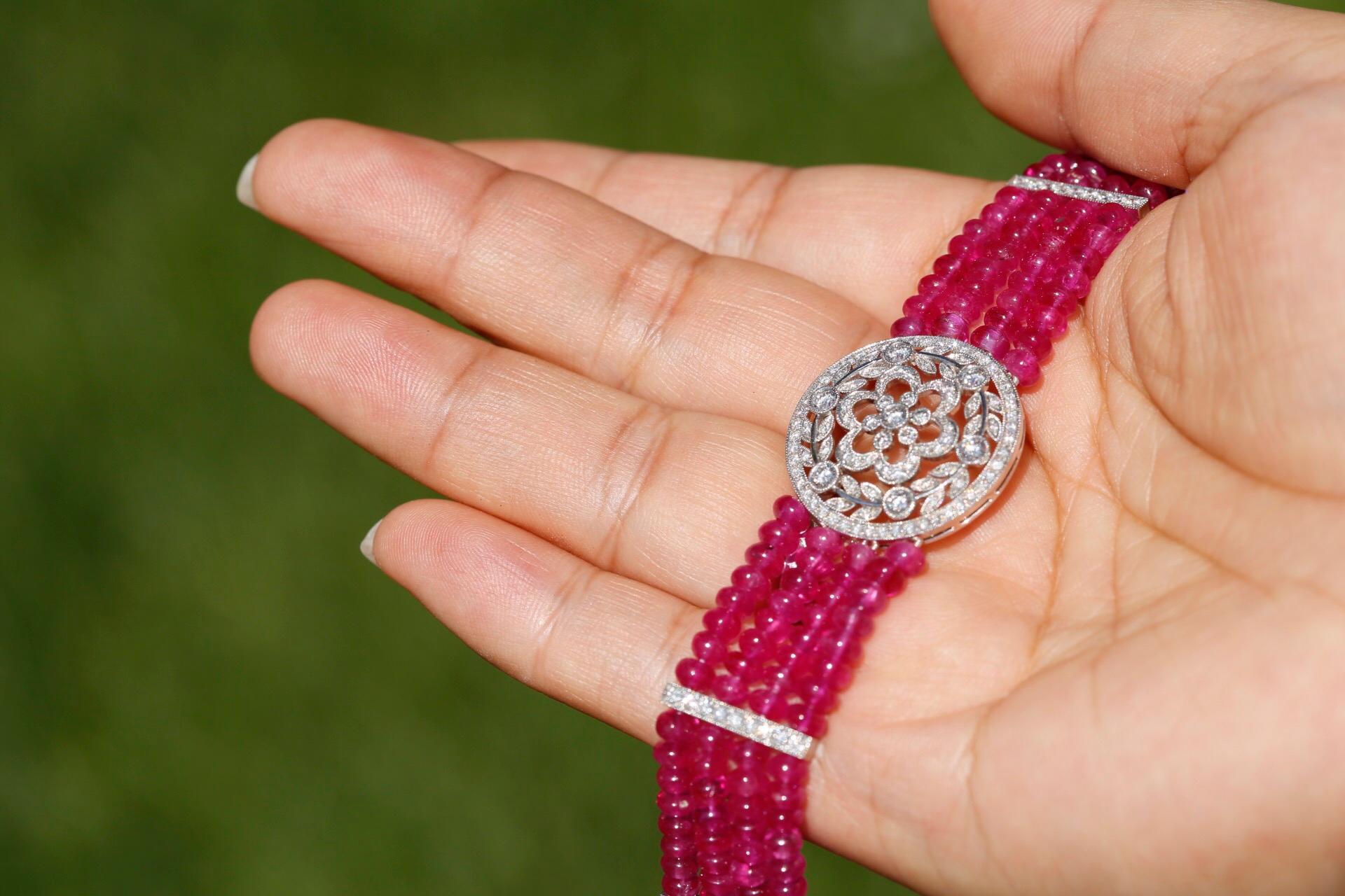 This bracelet is bursting with vivid berry colour, contrasted against the bright and lively diamonds glistening away.

The bracelet is made up of four strands of ruby beads separated with diamond spacers with a circular floral design at the centre