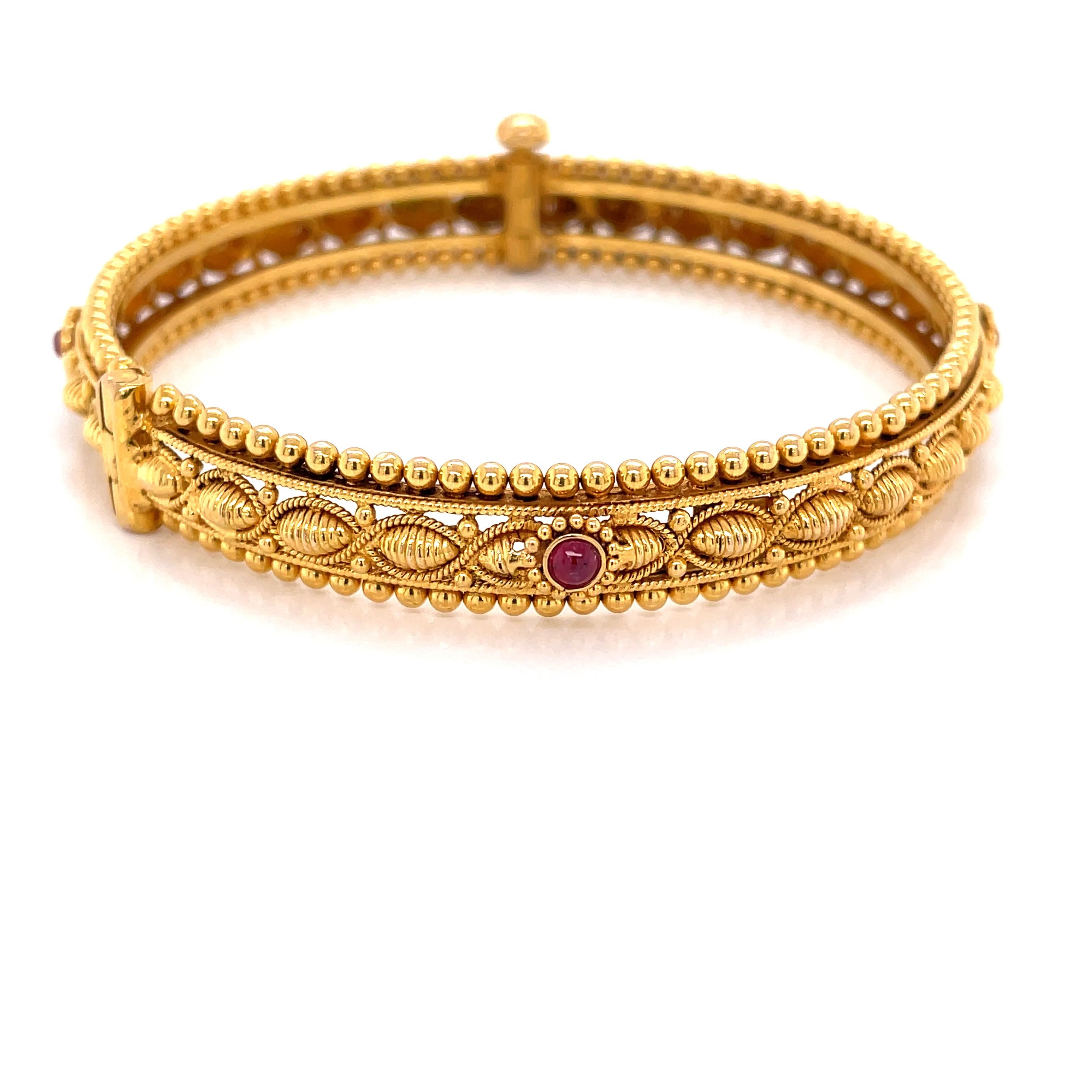 Elegant, in eighteen karat 18 karat yellow, artful gold filigree framed with delicate beads of gold create this stunning bangle bracelet. This fine piece presents four colorful natural cabochon ruby accents that are set along the inner ribbon of