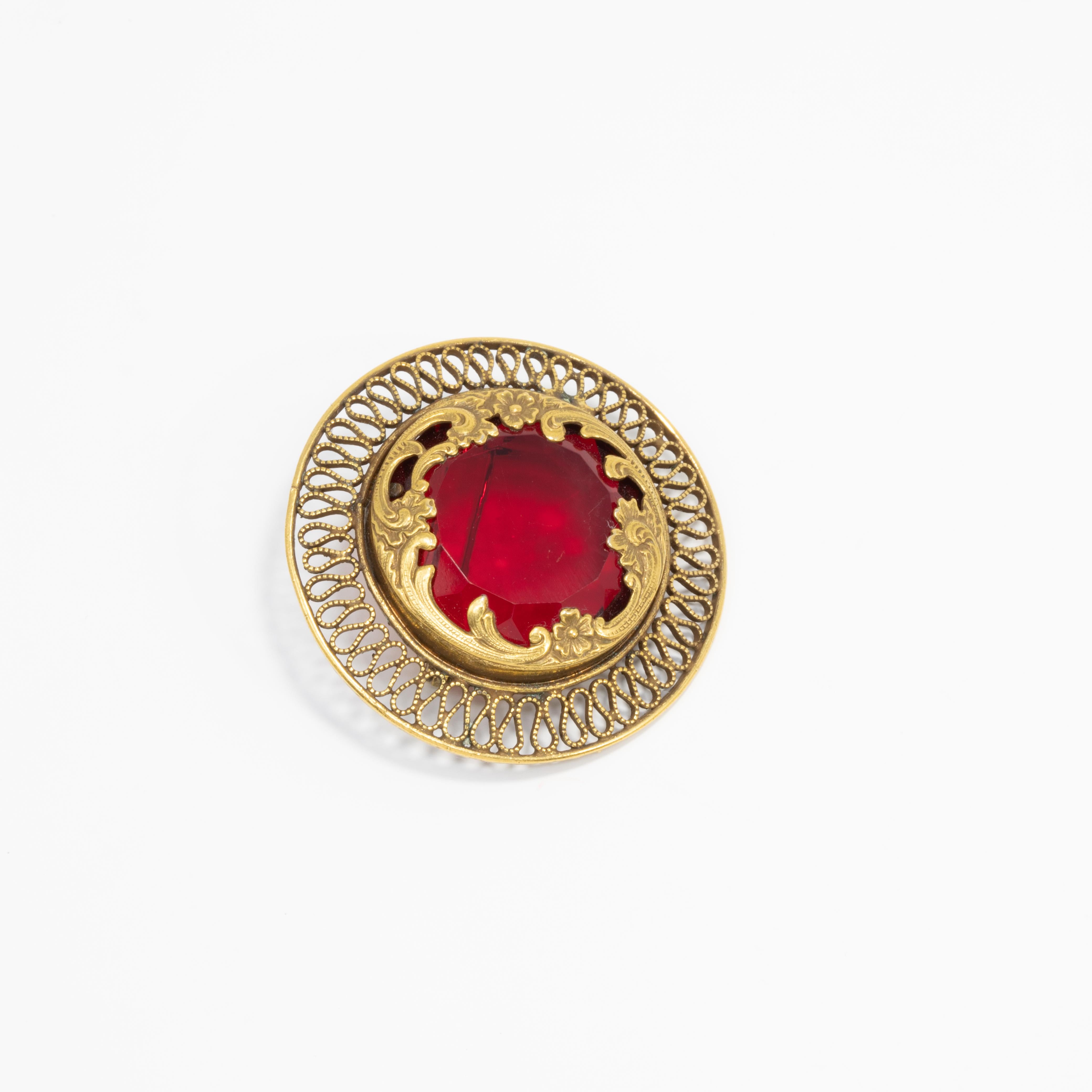 Vintage collectors' pin, featuring a bright, ruby-red crystal set in a round, open back, art-nouveau style, floral, setting in gold tone.

Mid 1900s.