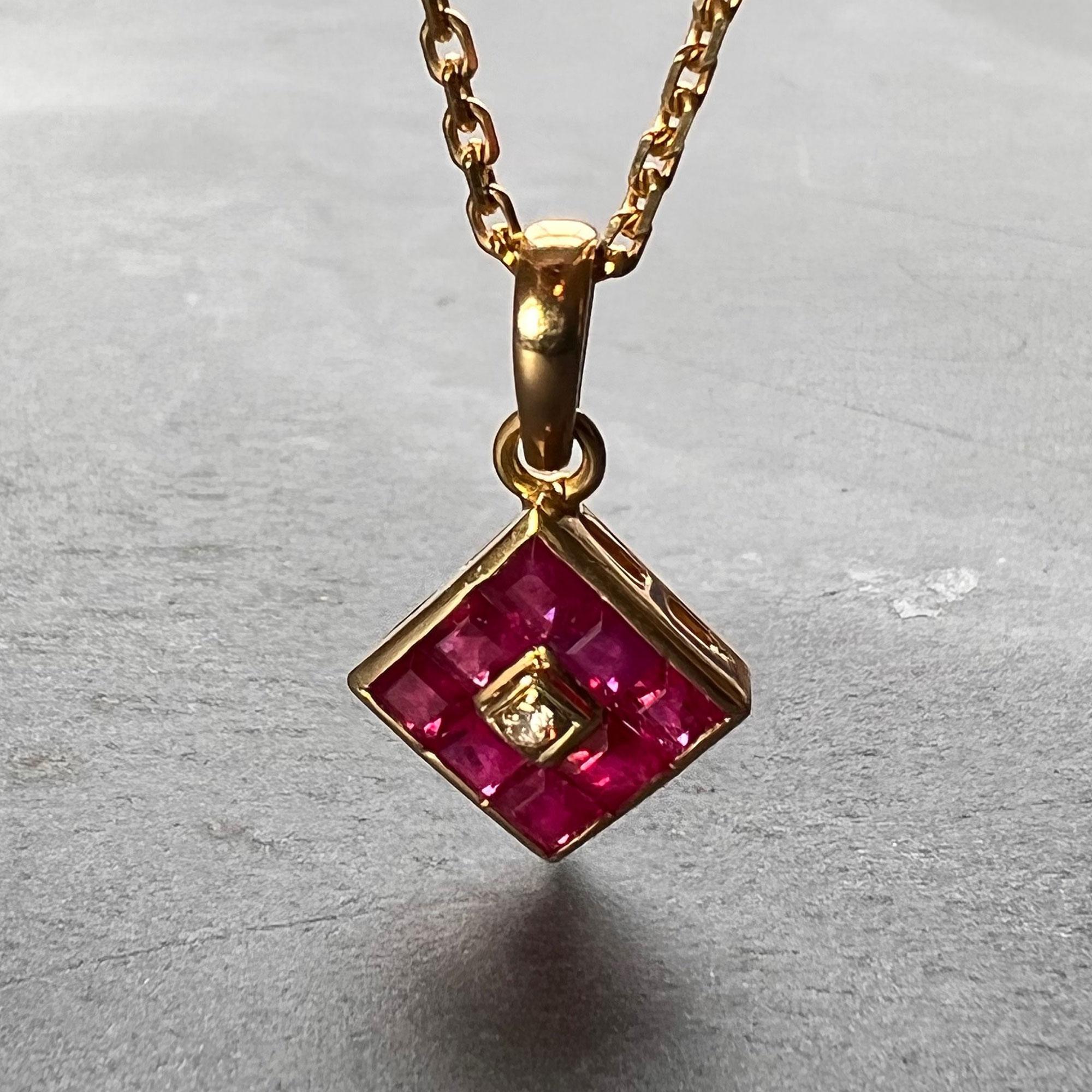 An 18 karat (18K) yellow gold cluster pendant designed as a yellow gold angled square set with eight red square cut rubies surrounding a round brilliant cut diamond. Stamped 750 for 18 karat gold to the inside of the pendant bail.

Diamond weight: